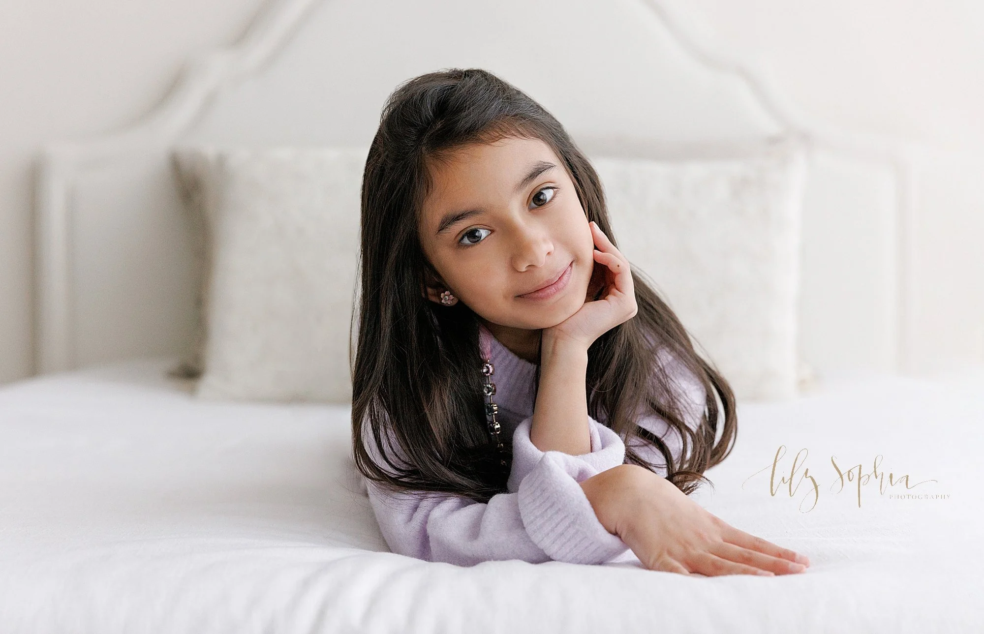  Family photography session with a young girl as she lies on her stomach with her right hand on her chin taken near Kirkwood in Atlanta in a photography studio that uses natural light. 