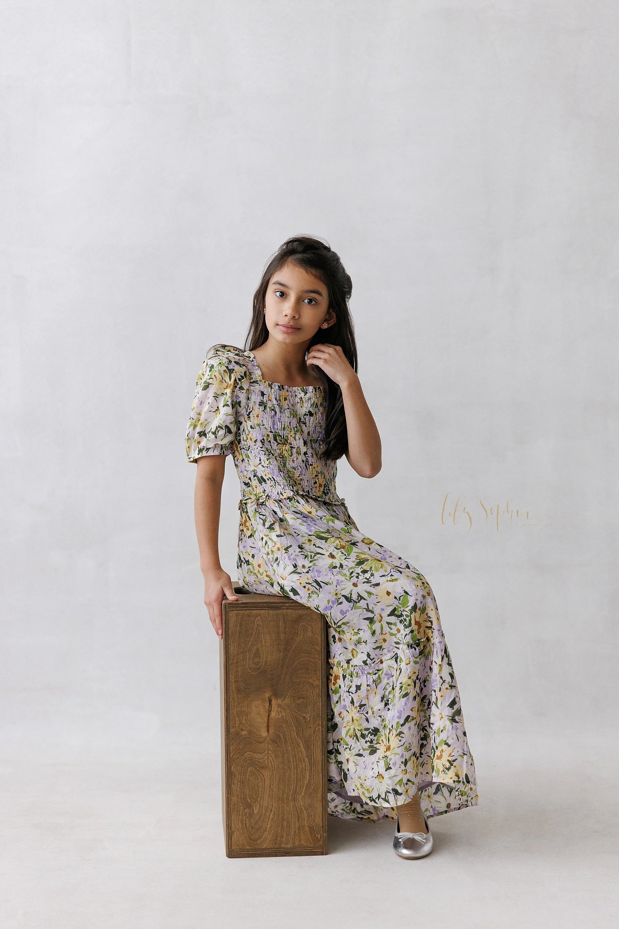  A girl sits on a wooden box in a natural light studio during a family photography session near Virginia Highlands in Atlanta, Georgia. 