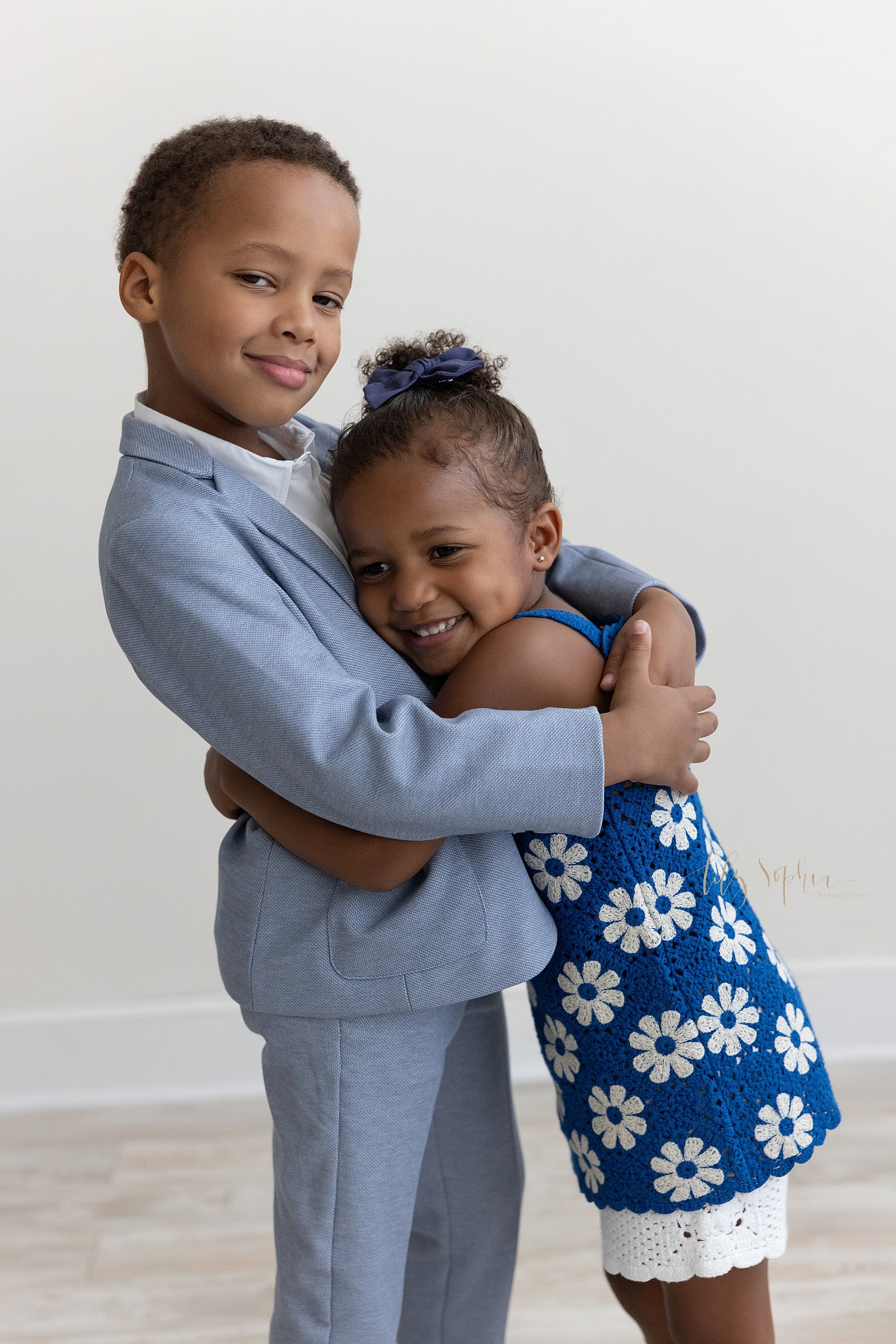  Family photo session with an African-American boy being tightly hugged by his younger sister as they stand in a photography studio near Virginia Highlands in Atlanta, Georgia that uses natural light. 