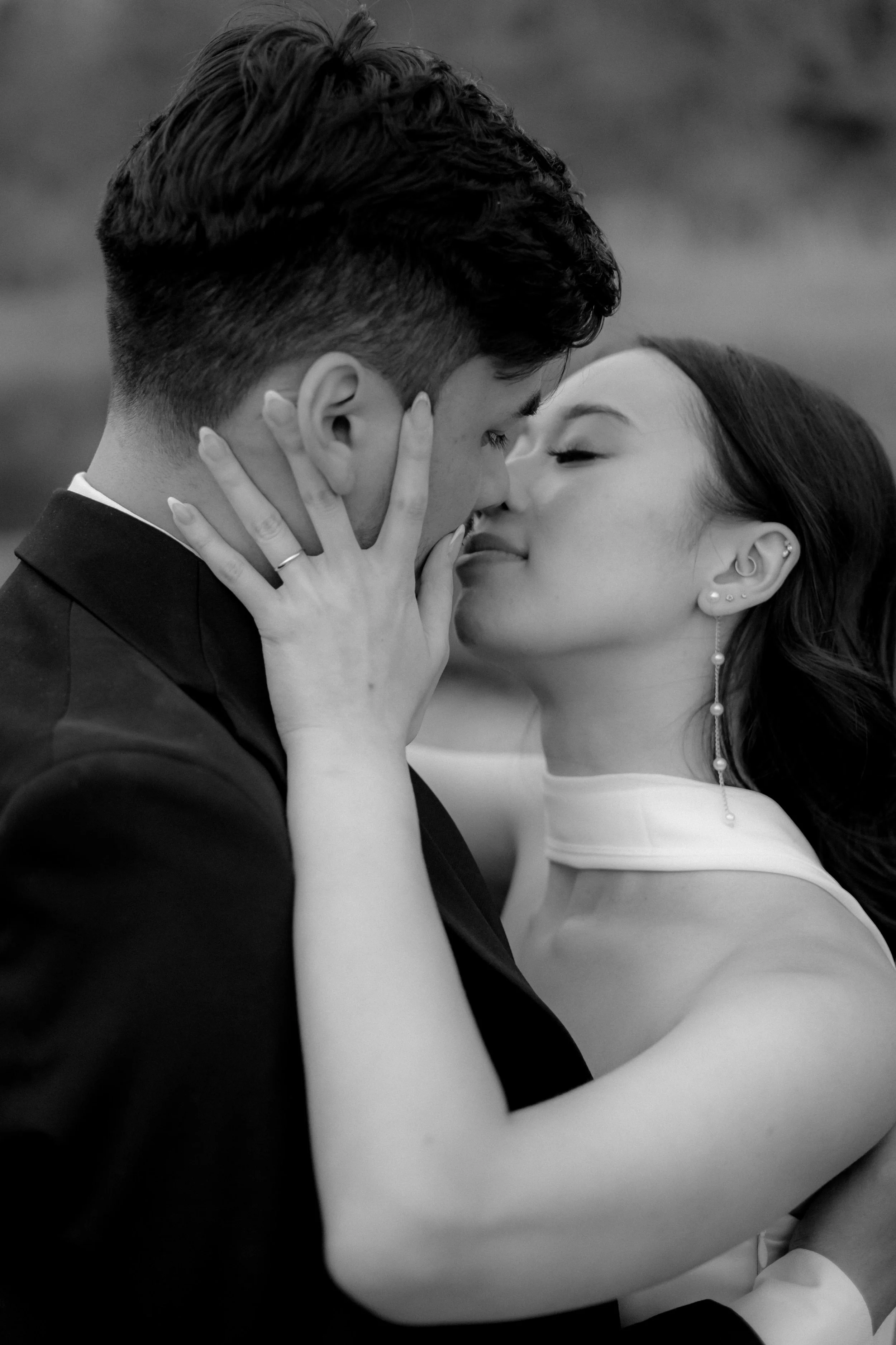 A black-and-white close-up photograph of a couple sharing an intimate kiss with their faces close, eyes closed, and hands touching each other's face.