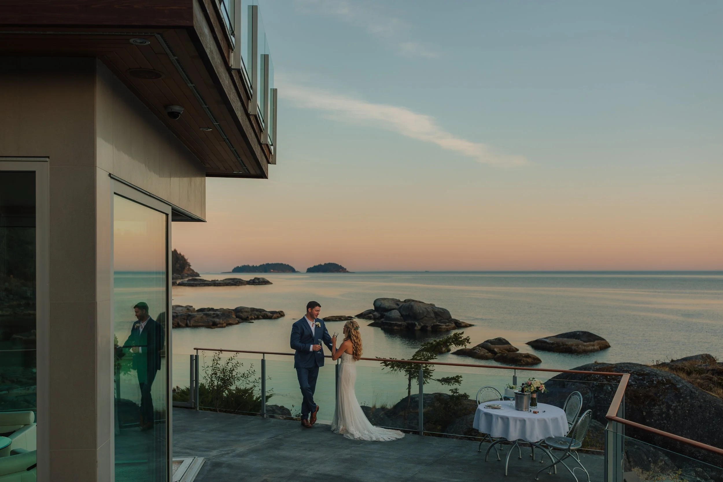 A bride and groom standing on a balcony overlooking the ocean at sunset, at the Pointhouse on the Sunshine Coast.