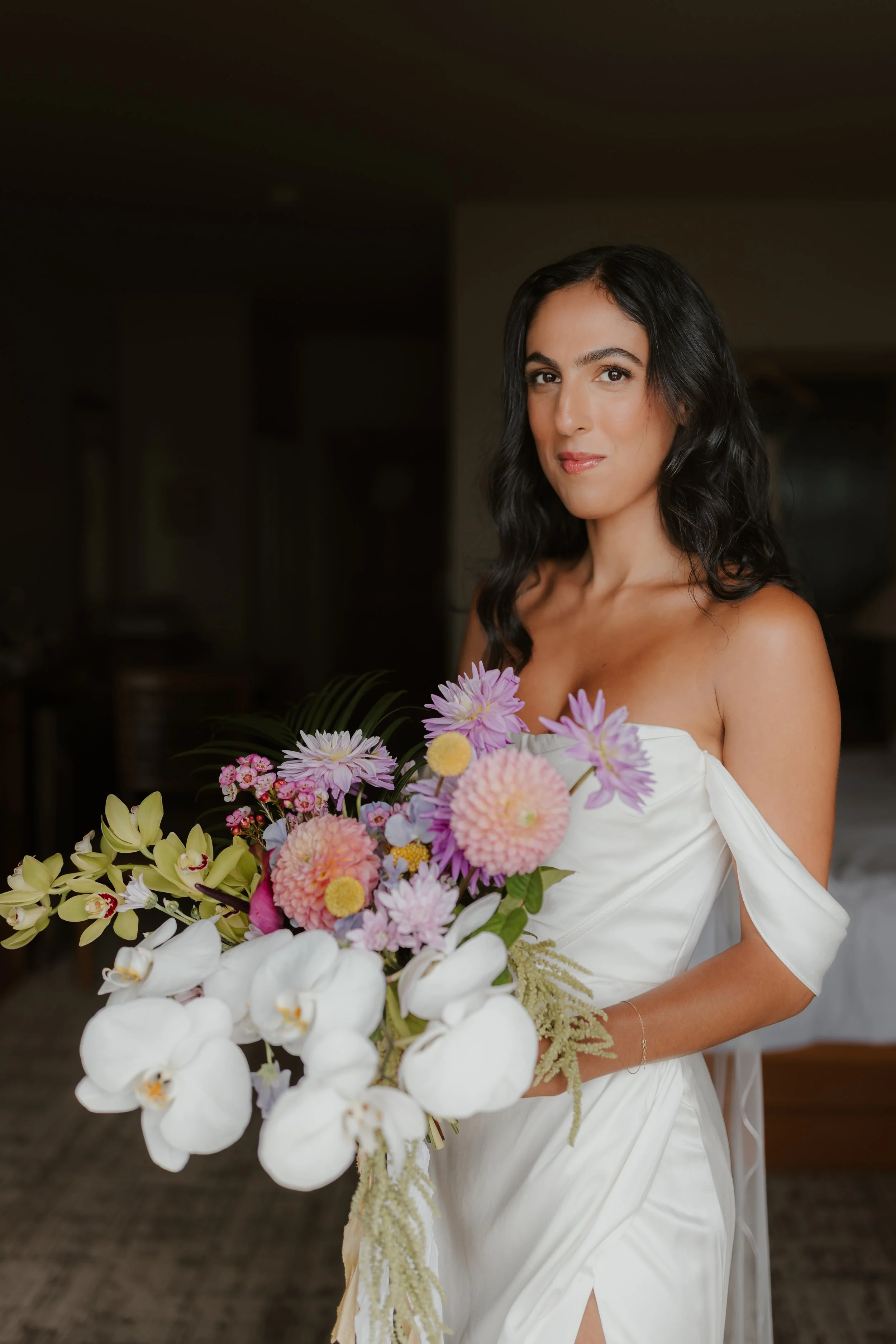 A woman in a white dress holding a large bouquet of colorful flowers, standing indoors at the Pacific Sands Resort in Tofino, BC