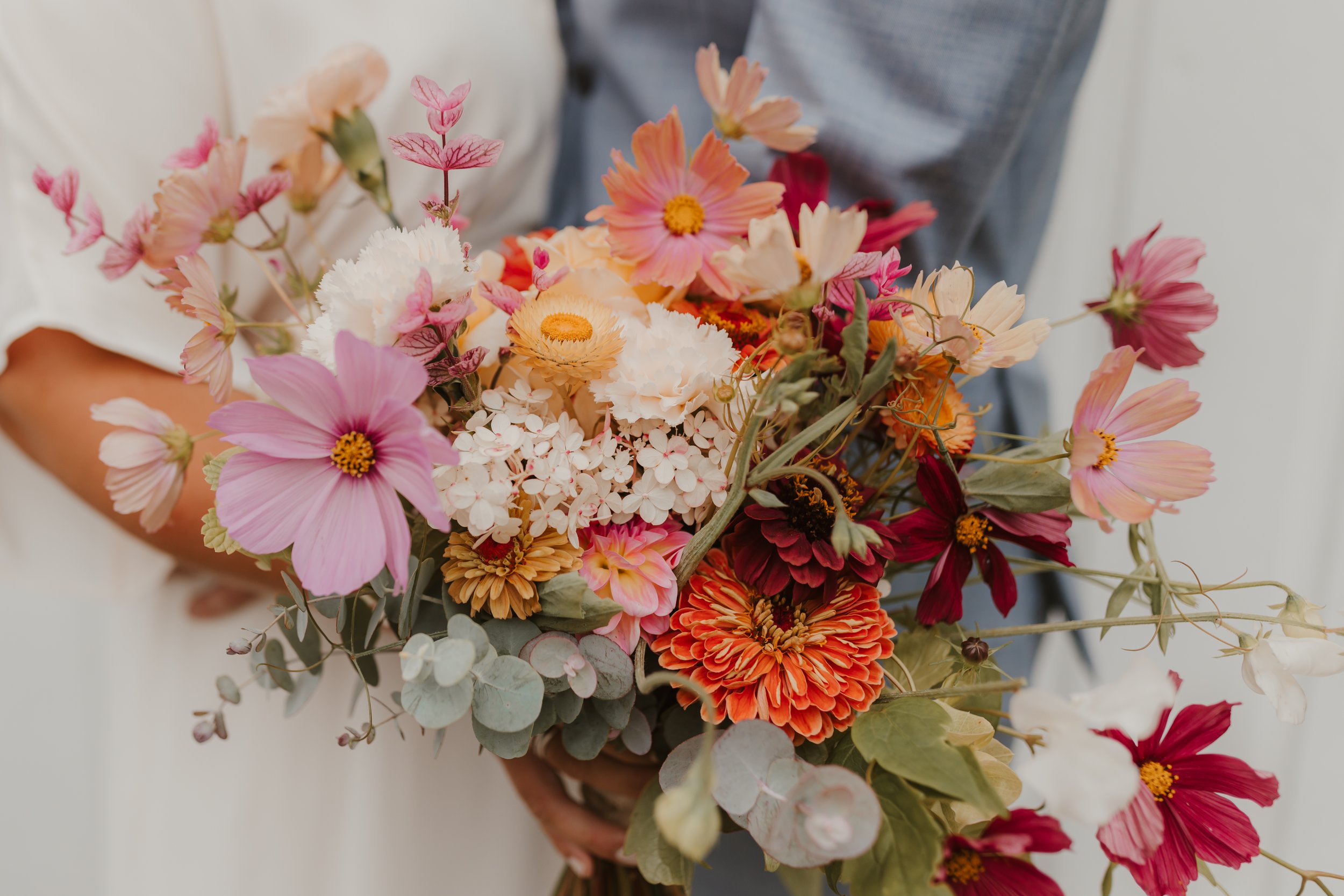 A bride holding a colourful bouquet of various flowers including pink, white, orange, and red blooms from Ruby's Run Urban Farm in Sechelt