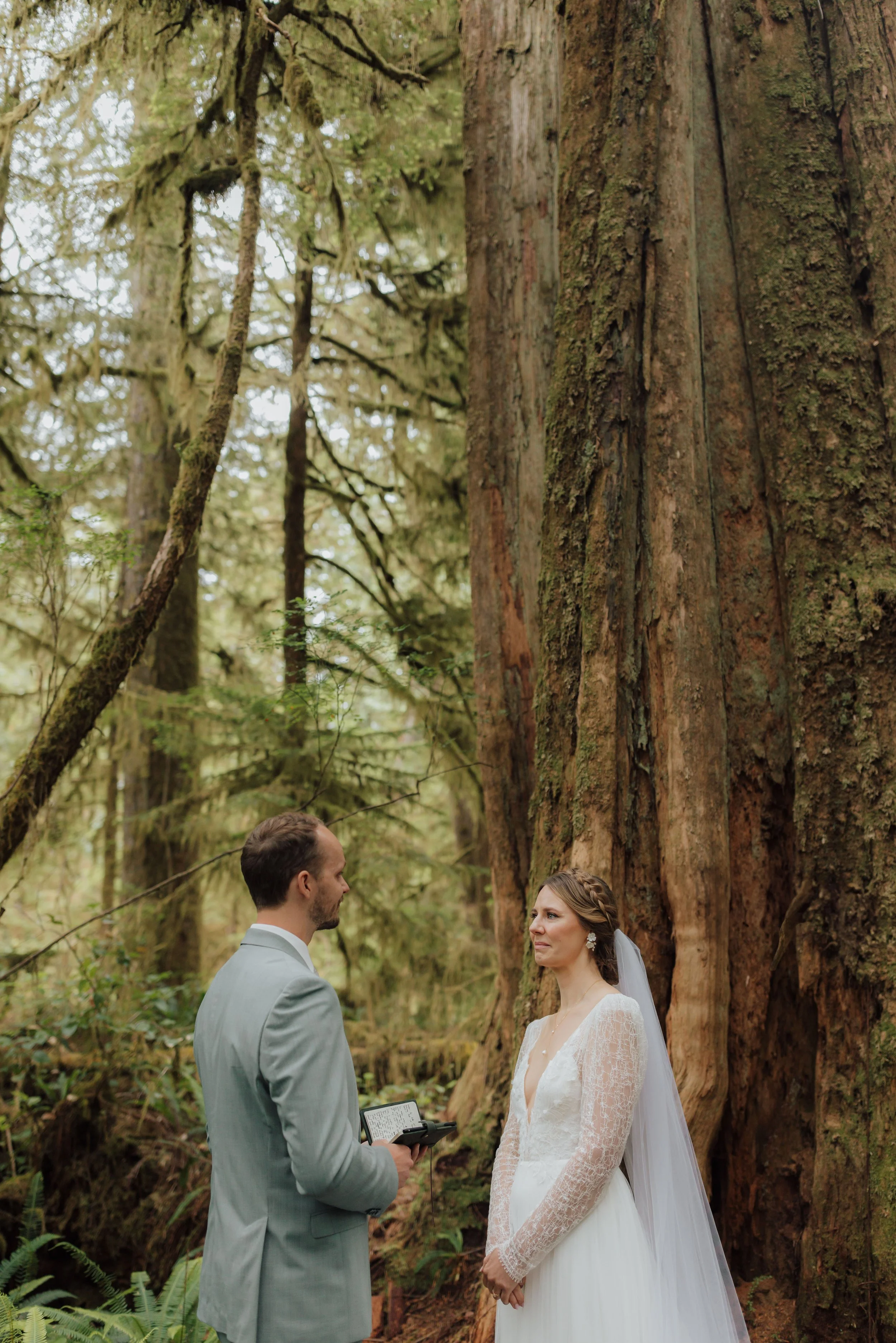 A bride and groom standing in a rain forest during their elopement ceremony reading their vows to each other in Tofino, BC