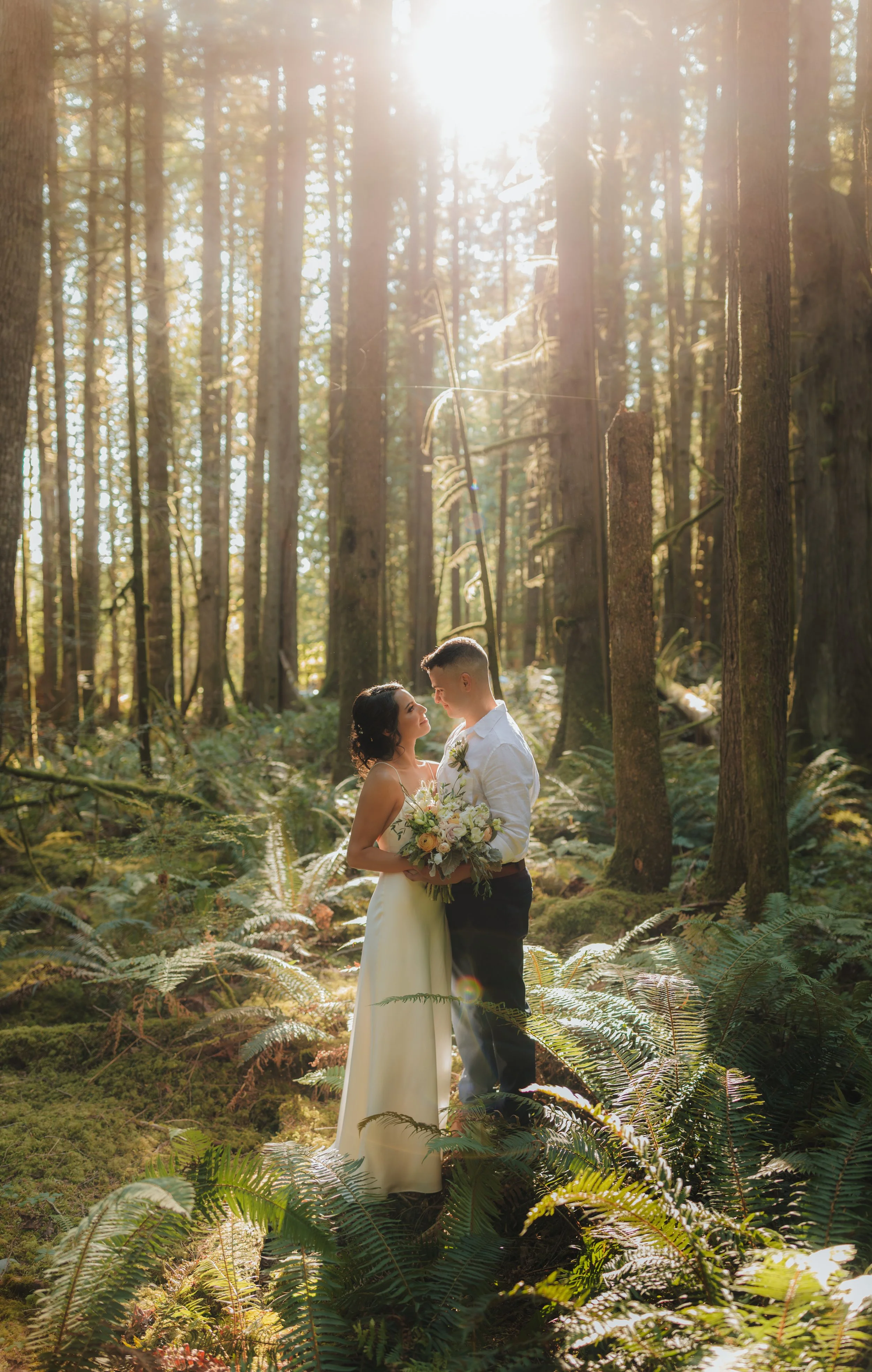 wedding couple facing each other in the rain forest with the golden light streaming through the trees in the Sechelt Inlet, Sunshine Coast, BC