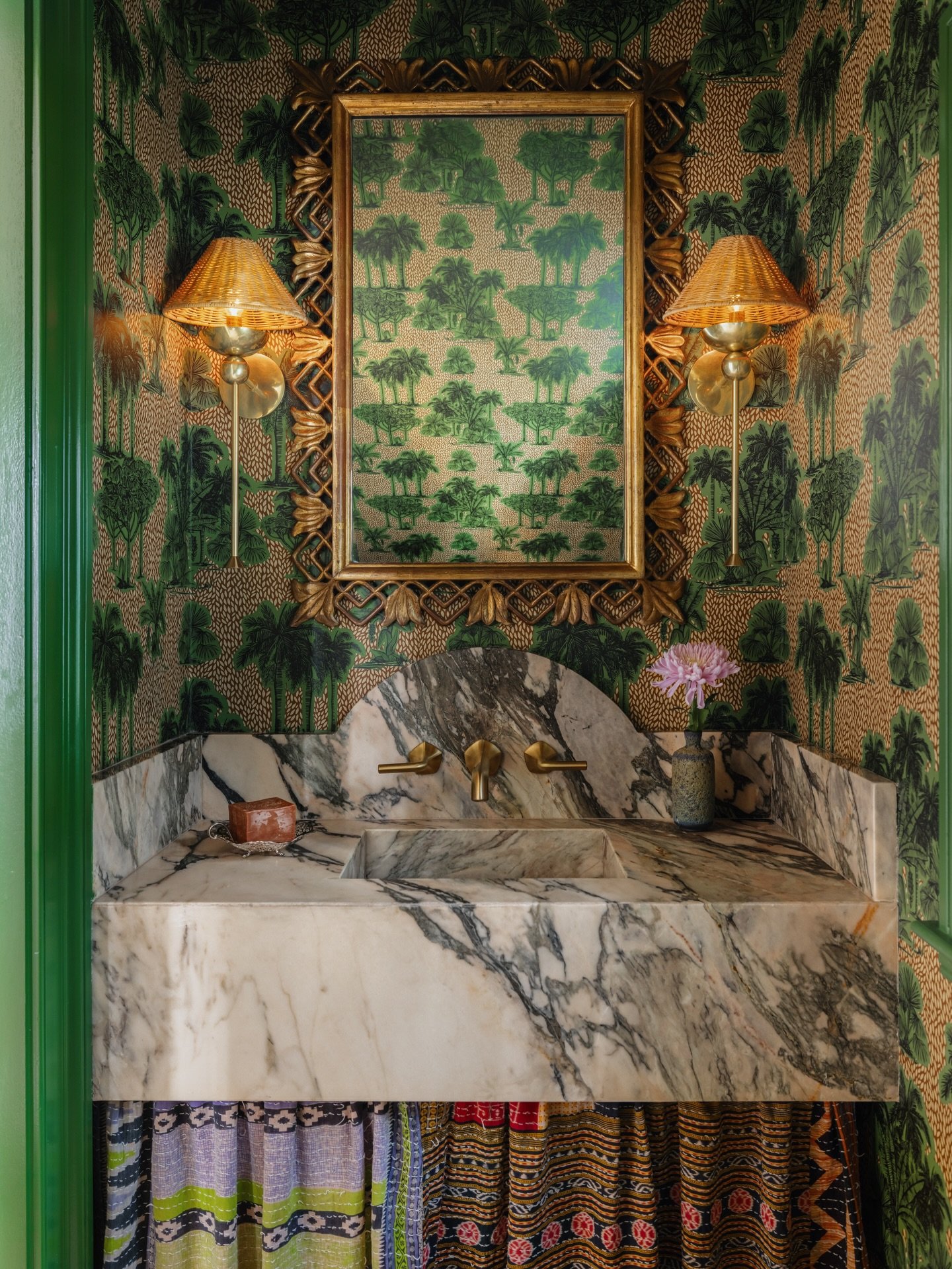 Tucked under the stairs, this powder room feels like stepping into a lush tropical garden. I&rsquo;ve always loved going maximalist in small spaces, so I started with this Tropical Safari wallpaper from @Backdrop. To bring in some soul, I sourced a g