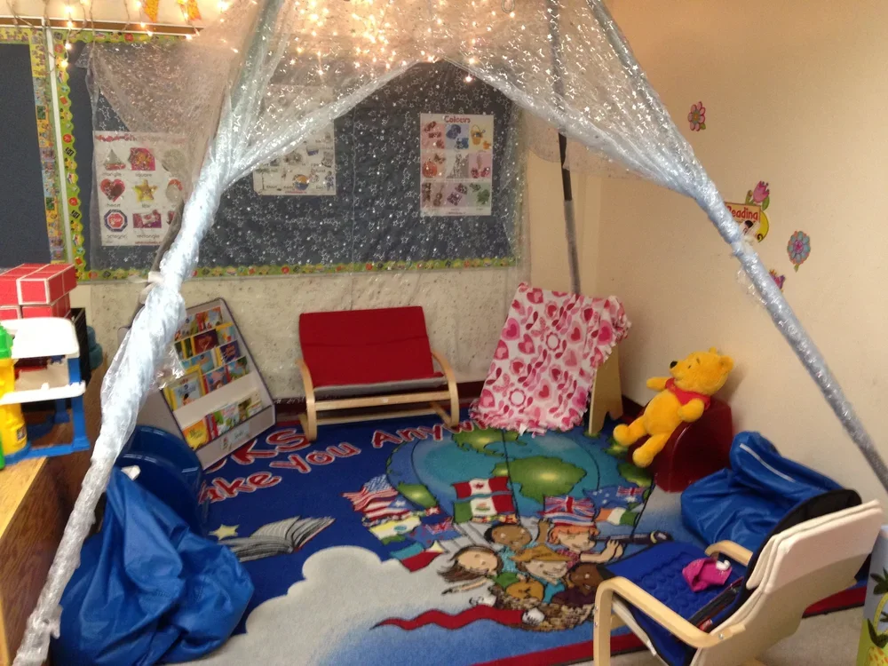 Children's reading and play area with a colorful cartoon-themed rug, a stuffed Winnie the Pooh, a small red bench, and a tent or canopy with transparent sides and glittery fabric.