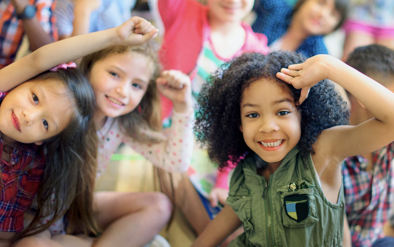 Smiling children of diverse ethnicities raising their fists and saluting in a group.