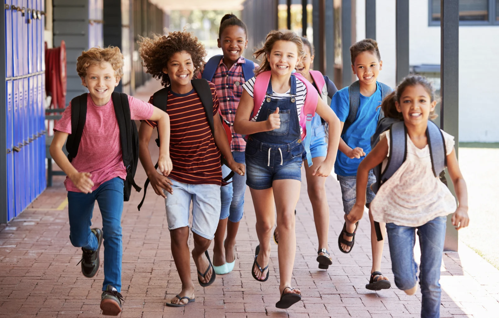Group of diverse smiling children walking outdoors at school, carrying backpacks.