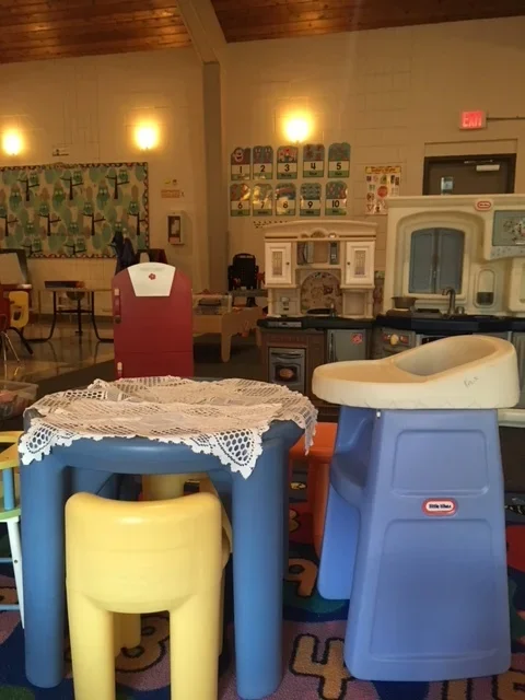 Children's play area with toy kitchen set, small table, and chairs in a classroom or daycare setting.