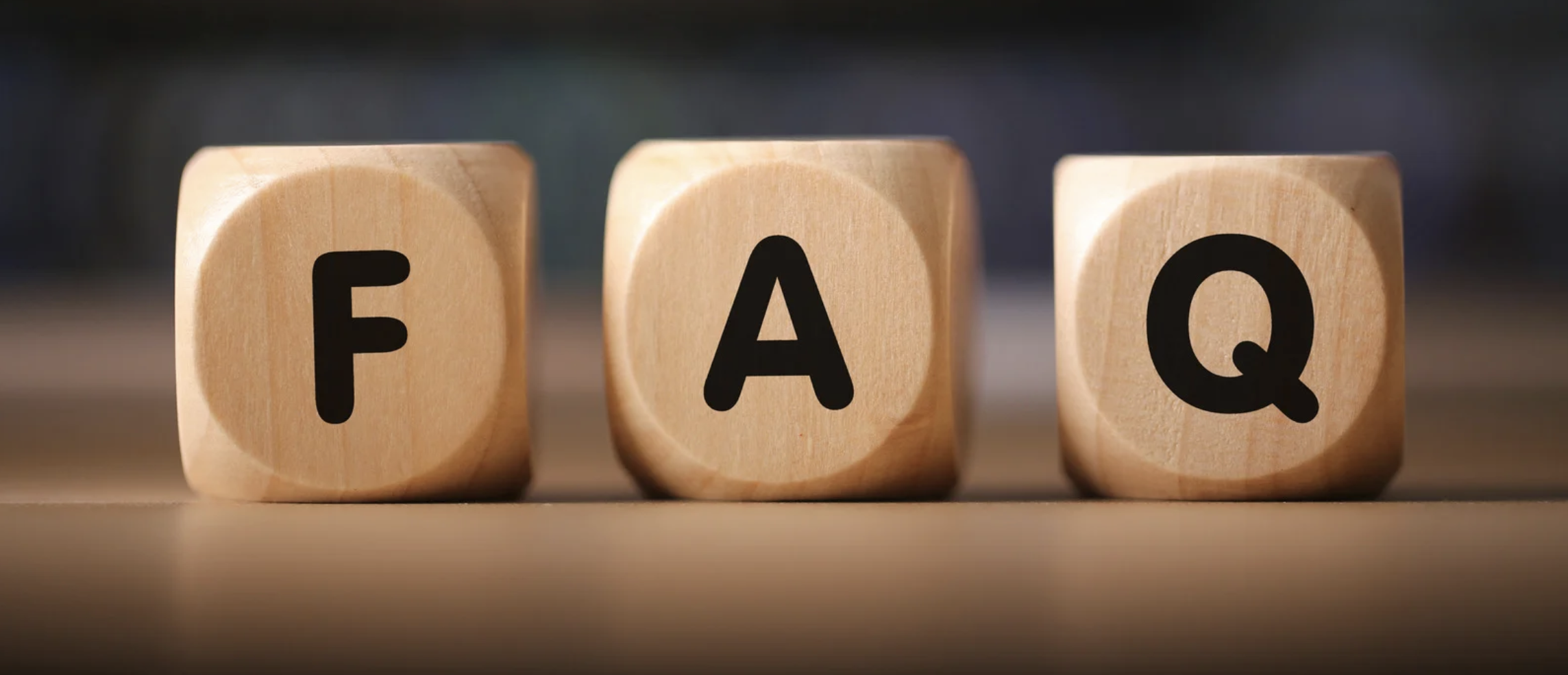 Three wooden blocks with black letters spelling out 'FAQ' on a wooden surface.