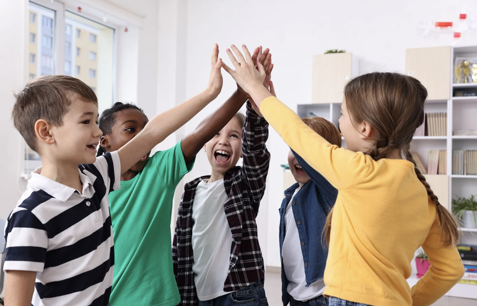 Group of five children giving each other high five in a classroom.
