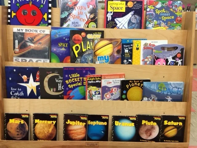 Books about space and planets on a bookshelf, including titles about Mars, Mercury, Jupiter, Neptune, Uranus, Pluto, and Saturn.
