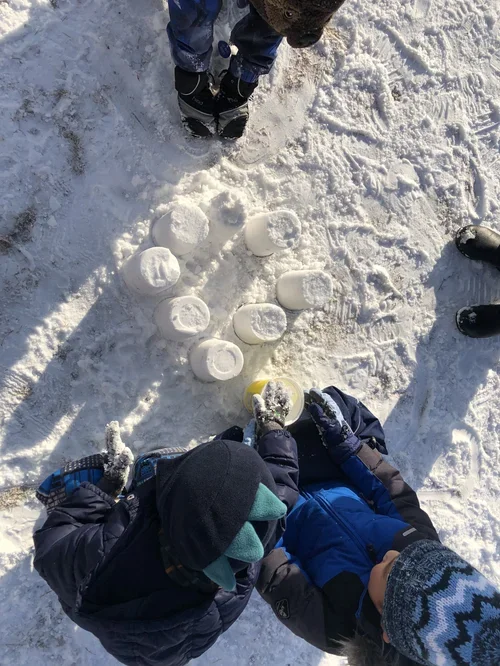 Children building snowmen outdoors in winter, surrounded by snow, with snowballs in the snow.