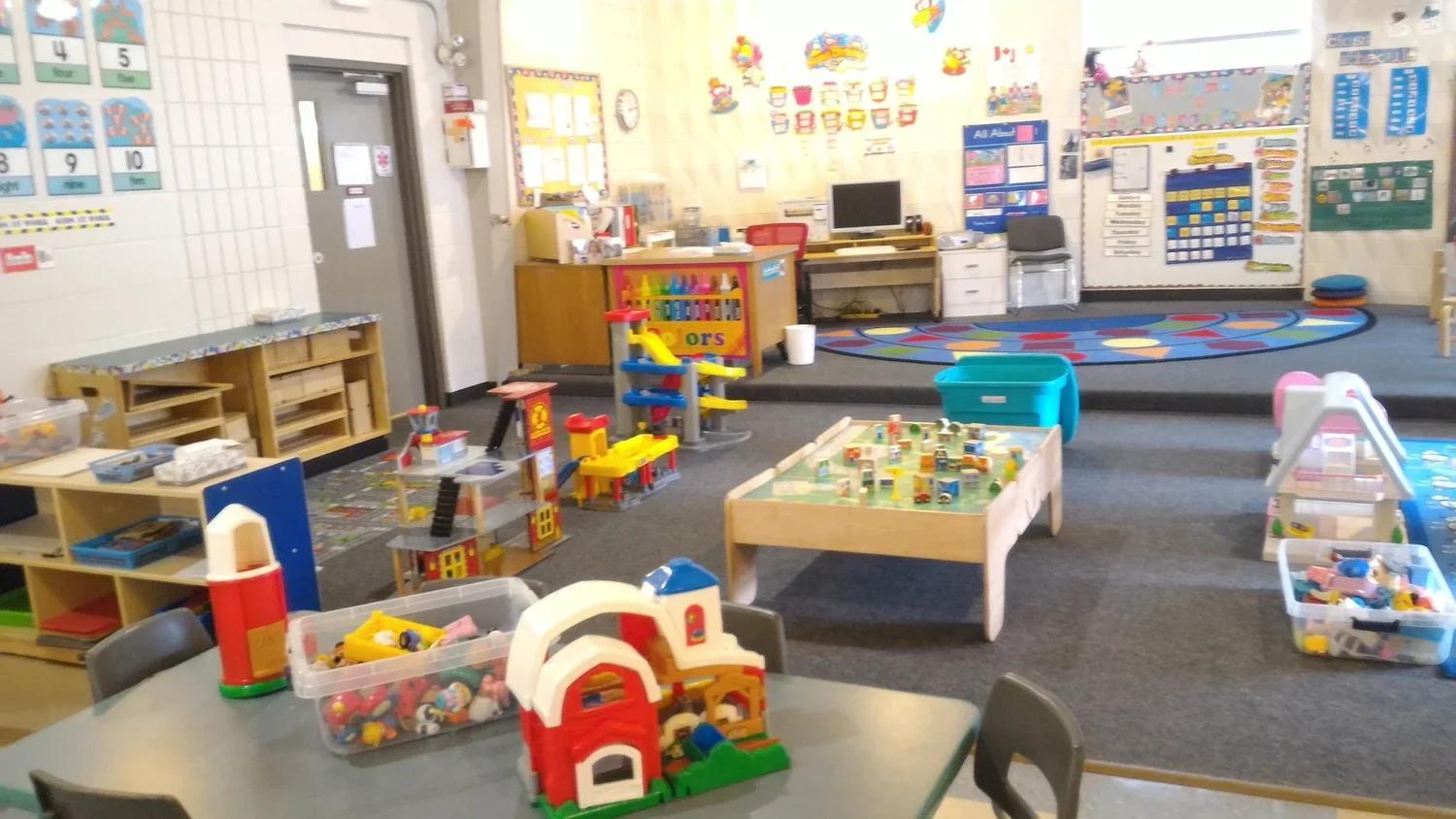 A colorful school classroom with toys, play furniture, and educational posters on the walls.