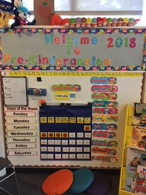 Pre-kindergarten classroom bulletin board with colorful alphabet, days of the week, months, and a calendar, decorated with Sesame Street characters.