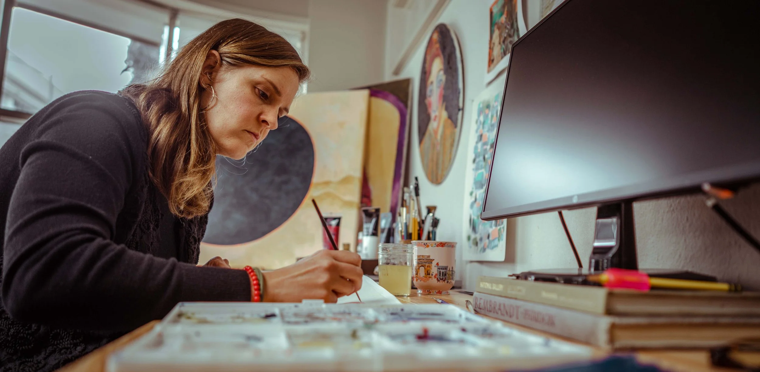 annie draws at a desk withc olorful paintings around her