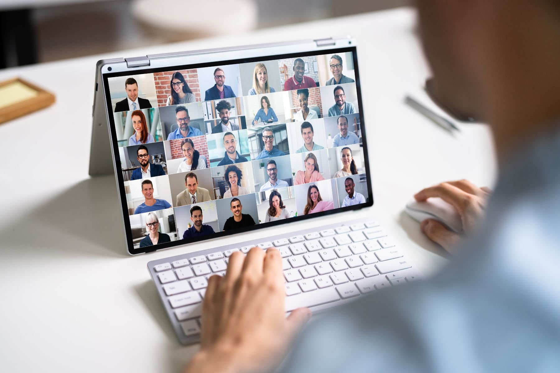 Person participating in a virtual meeting on a tablet, with a grid of diverse smiling individuals in a video call.