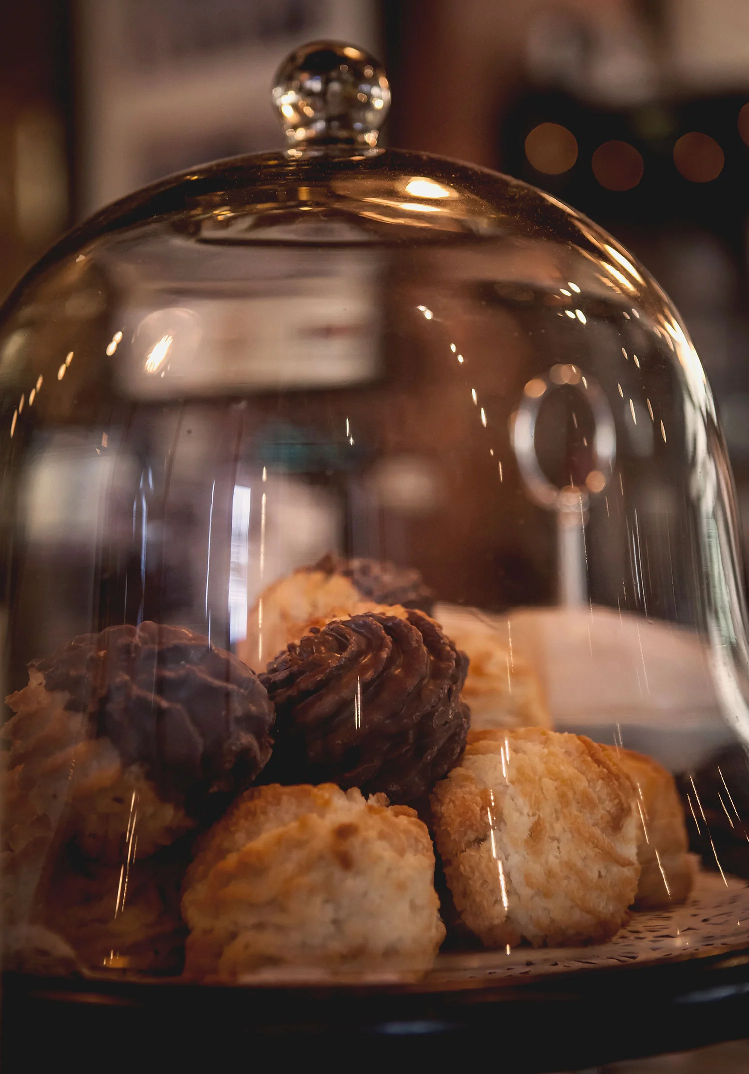 Assorted cookies under a glass dome on a plate, with a blurred background.