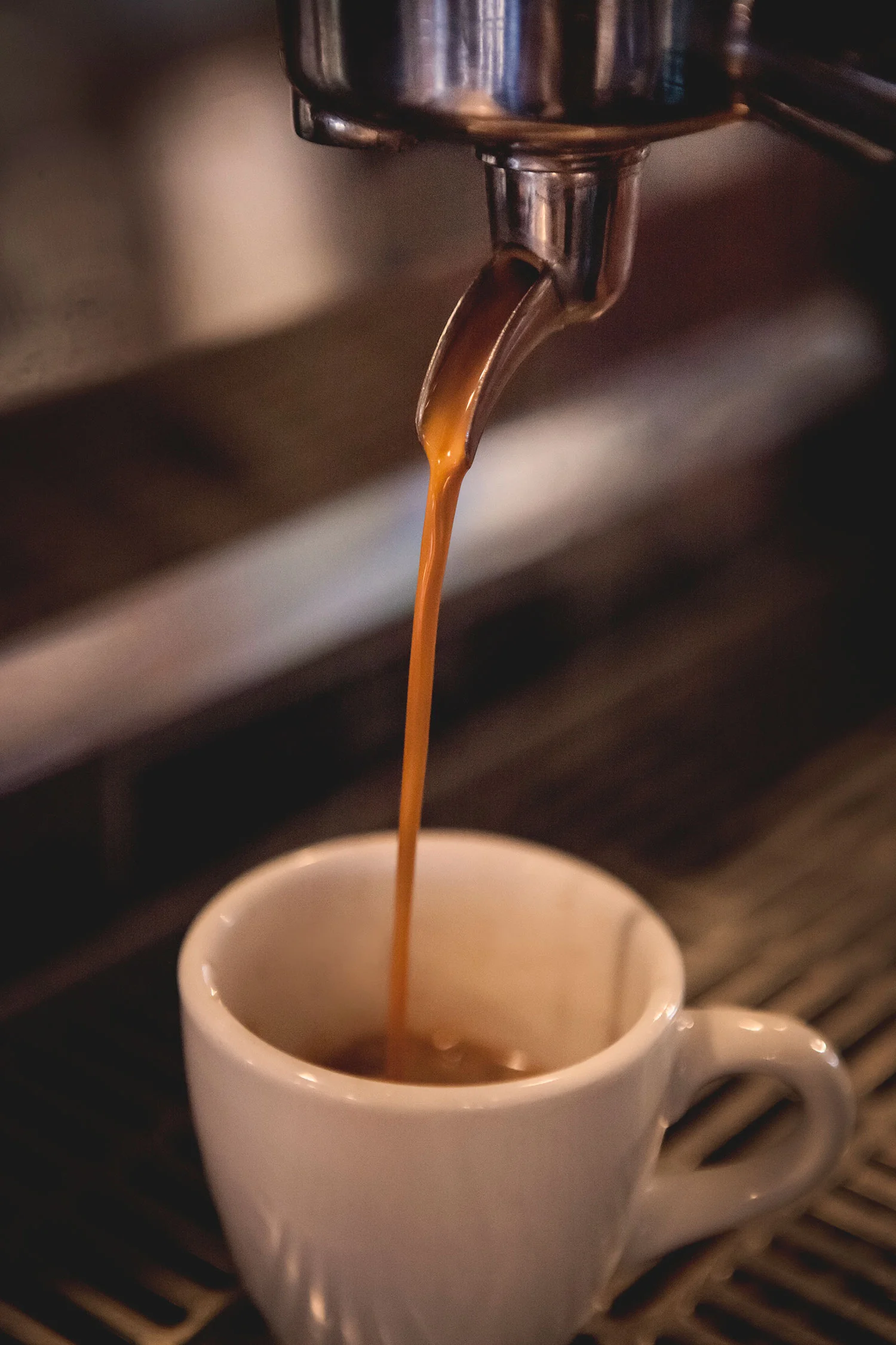 Coffee being brewed from an espresso machine into a white ceramic cup.