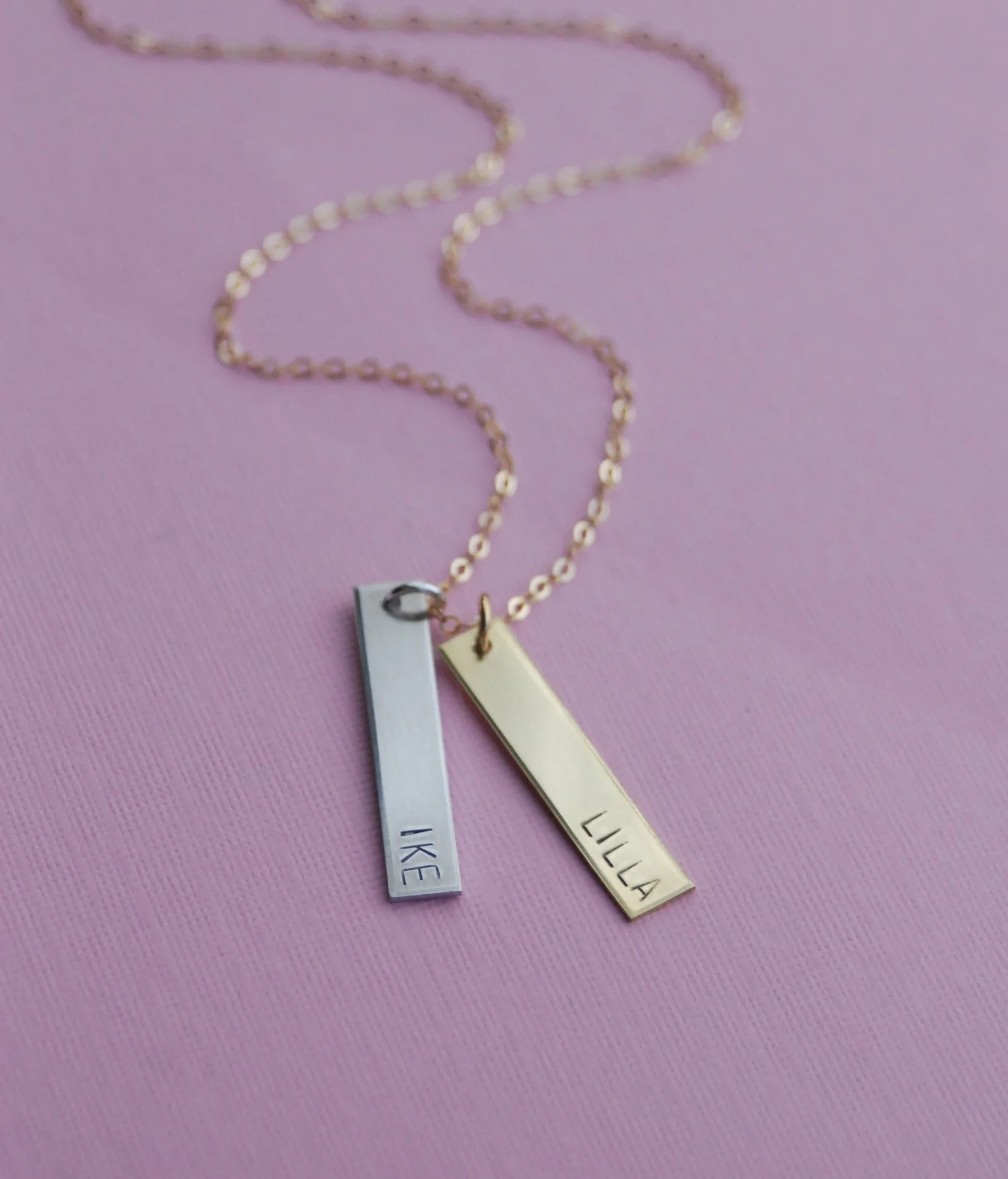 A necklace that has a vertical stamped rectangle that says "ike" and one that says "lilla"
