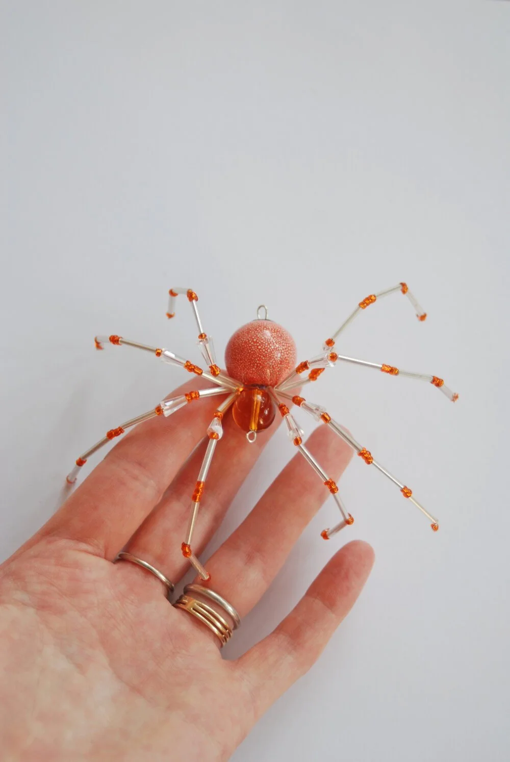 a hand holds out a wiry spider made of clear and gold beads