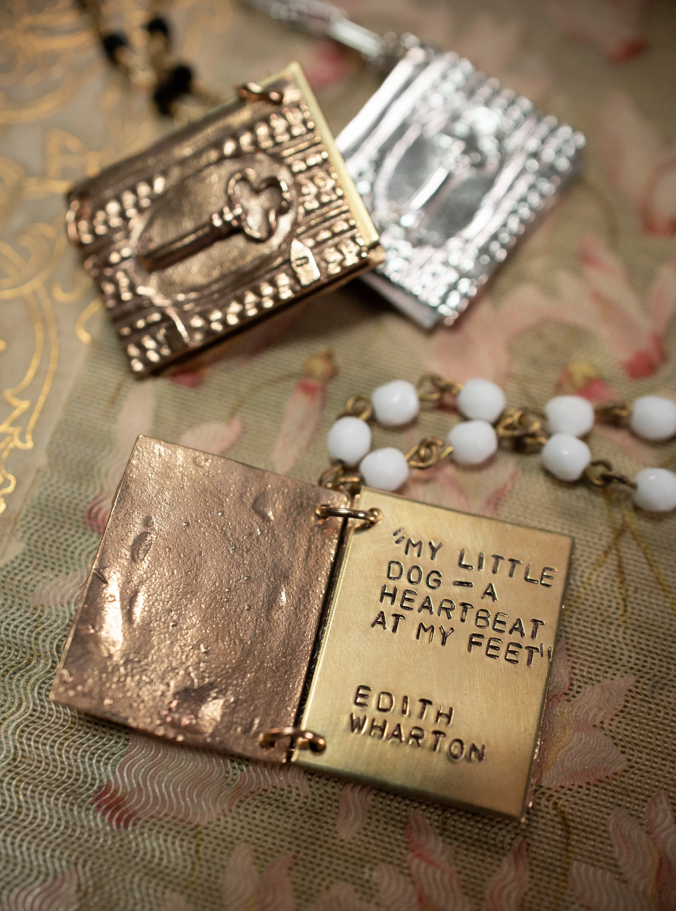 A pendant shaped like a book is open to a brass page with an Edith Wharton quote