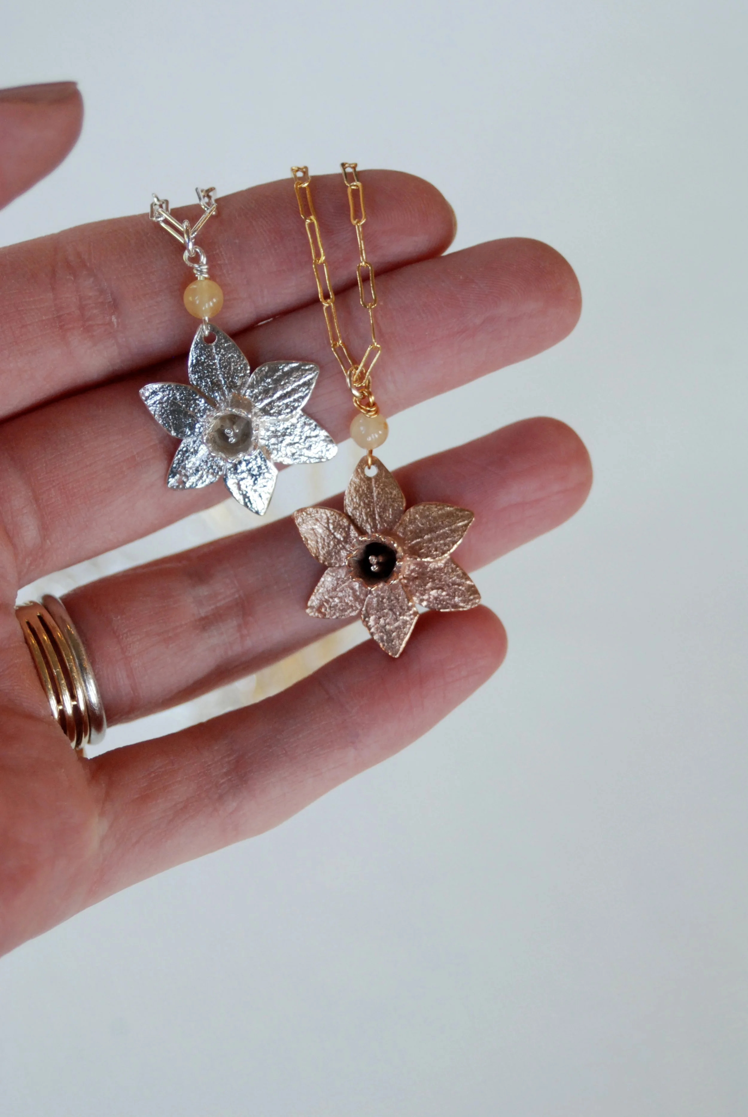 A hand holds out a silver and godl necklace with a pendant shaped like a daffodil flower