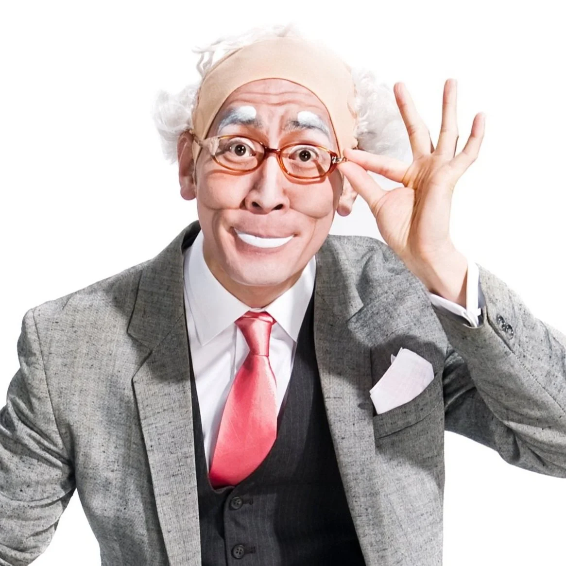 A cheerful man with white hair, glasses, and a gray suit with a pink tie, adjusting his glasses with a playful expression.