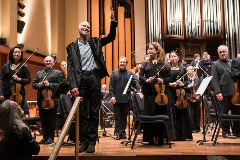 Adams, arm raised, takes a bow with the Seattle Symphony Orchestra.