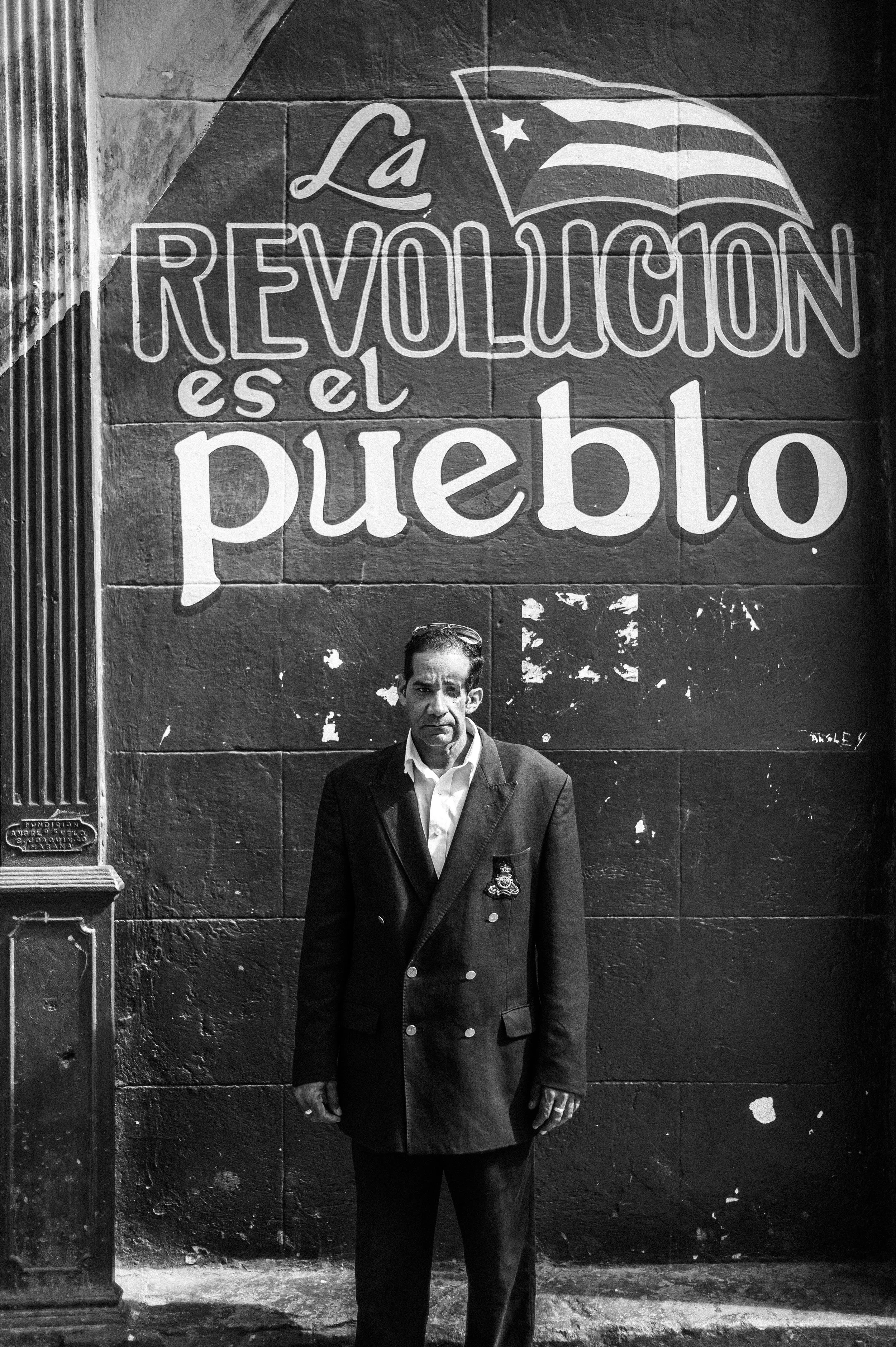 I first saw Orestes walk past me in a rugged part of Havana. He walked into a fruit market as I walked out, and he caught me staring at him with his one eye. I froze at that moment. I became so intrigued by how well taken care of he looked that I had to go up to talk to him. Orestes lost one of his eyes in a motorcycle accident when he was twenty and he received free health care services to fix it, provided for all citizens by the government. He told us he works for the State bus company and that he is pleased with his job. When I asked him what he thought about Fidel and his policies, Orestes said that he was loyal to him, that he is a "fidelista." We asked him to stand against this mural, "La Revolucion es el pueblo", because despite Fidel's death, like many others in this small neighborhood, Orestes continues to believe in his patron and the way of life Fidel has planted on this small patch of land.