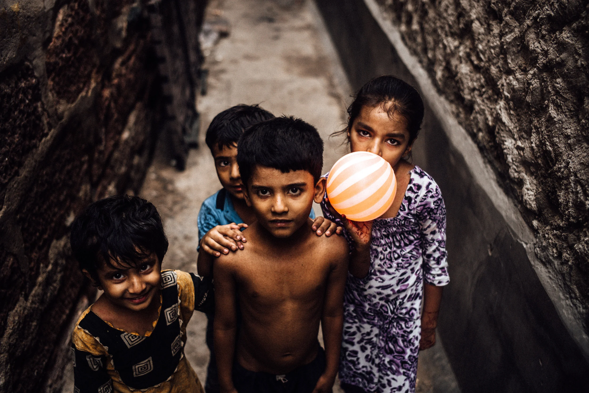 I took this photo while walking down an alleyway in Old Jodhpur, India, commonly referred to as the Blue City of Rajasthan. While exploring the labyrinth of streets in the ancient city, I found something spectacular around each and every corner. It was my last day in the city and I was eager to continue documenting the people and it’s culture. Luckily, the people around me were even more eager to have their photos taken. This photo of children portrays the nature of the people and culture I experienced in India. The boy in the center, shirtless and street-wise like many other children in India, has wrestled his way to the front of the group. The girl, hiding her face behind the luminous ball, suggests the way women of India veil their faces with the end’s of their sari’s. The smile of the young boy dressed in yellow mirror’s the friendliness and warmth of the Indian culture, which I am so grateful to have experienced. Finally the young boy in blue in the back of the group places his hands on the shoulders of his comrade, illustrating the support and respect Indian people have for one another. 