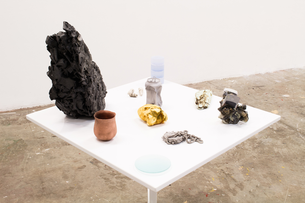  On the Beach,&nbsp;2015, 34"x34"x48", plastic, resin, graphite, clay, sand, gold, aluminum, copper, chrome, nickel, glass, fossil gastropods, fossil shark teeth, foam, silica, wristwatch packaging, Motorola Razr, steel folding table 