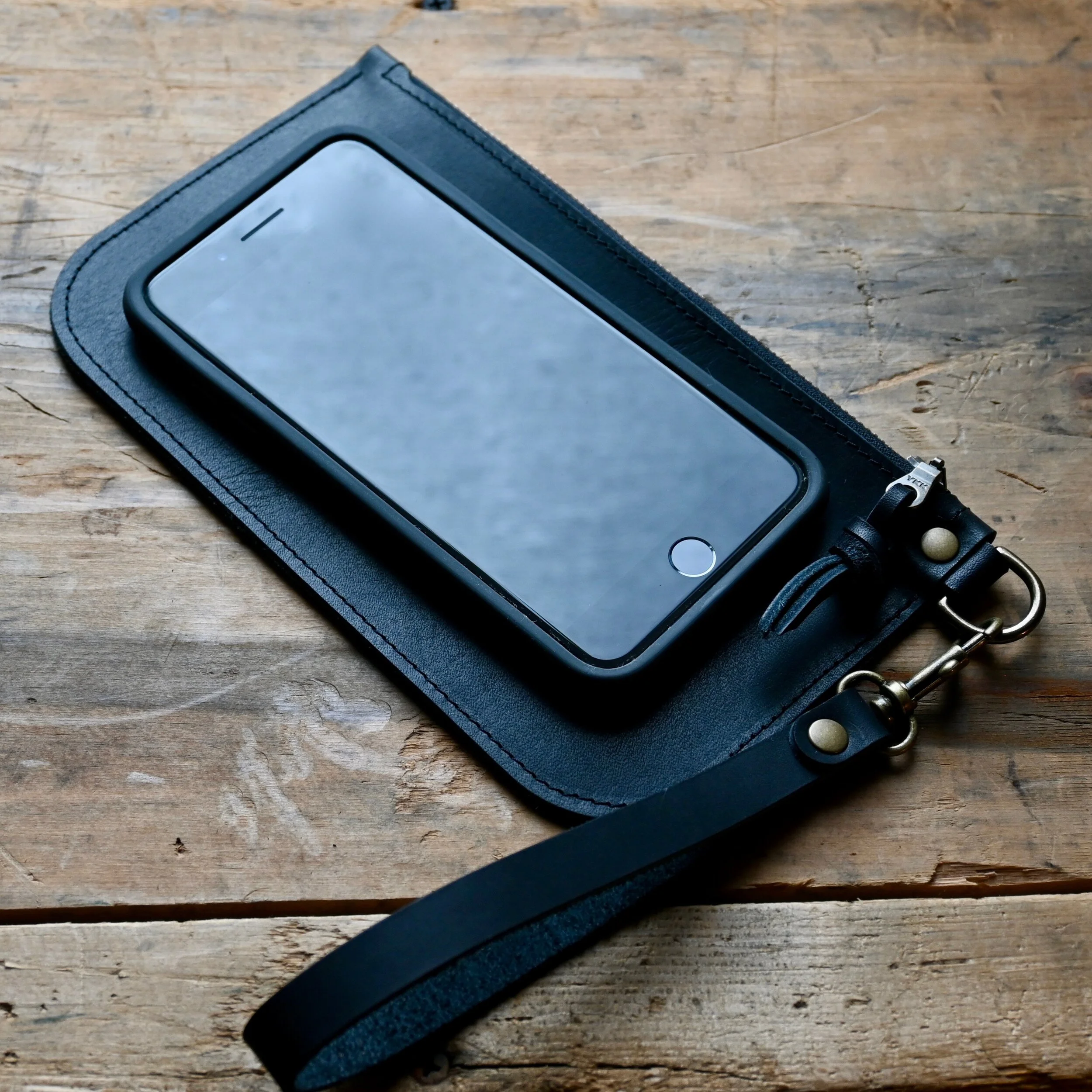 A small black pebbled leather clutch with a cellphone layed over it so it is clear that a small cellphone will fit in the bag.
