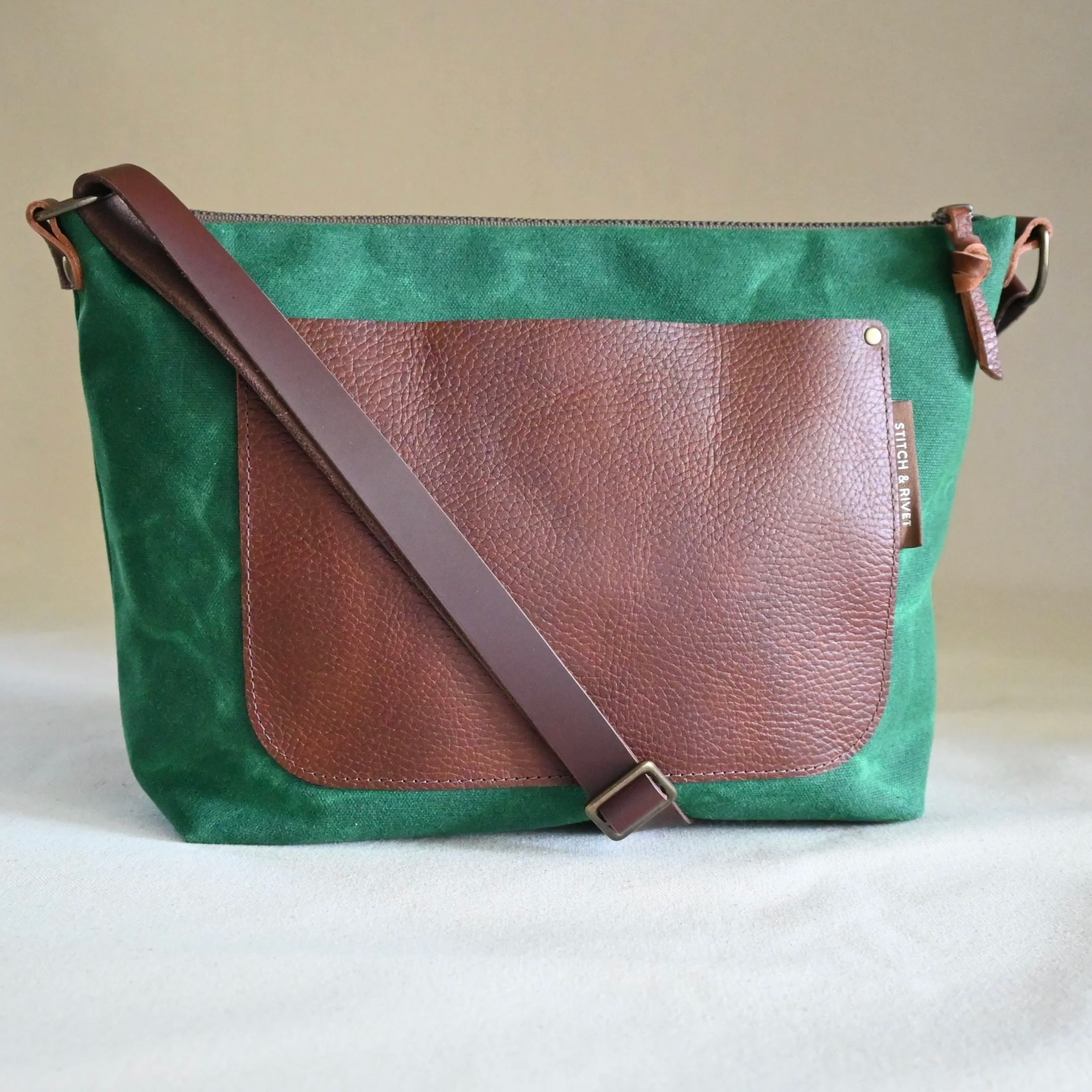 A Kelly green (bright green) waxed canvas and brown leather Day Bag on a beige backdrop.