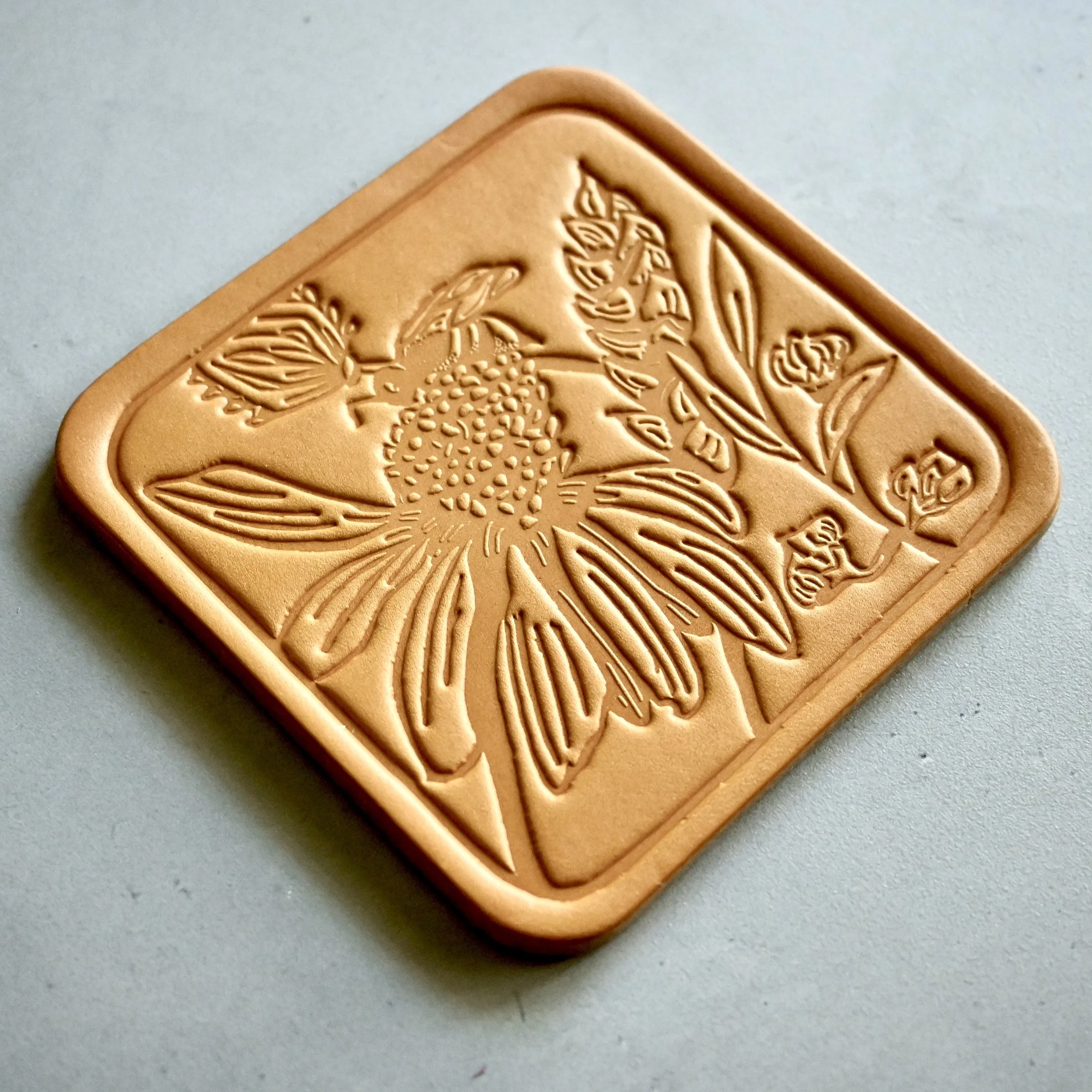 Leather coaster with coneflower, wheat stalk, flower buds and bee.JPG