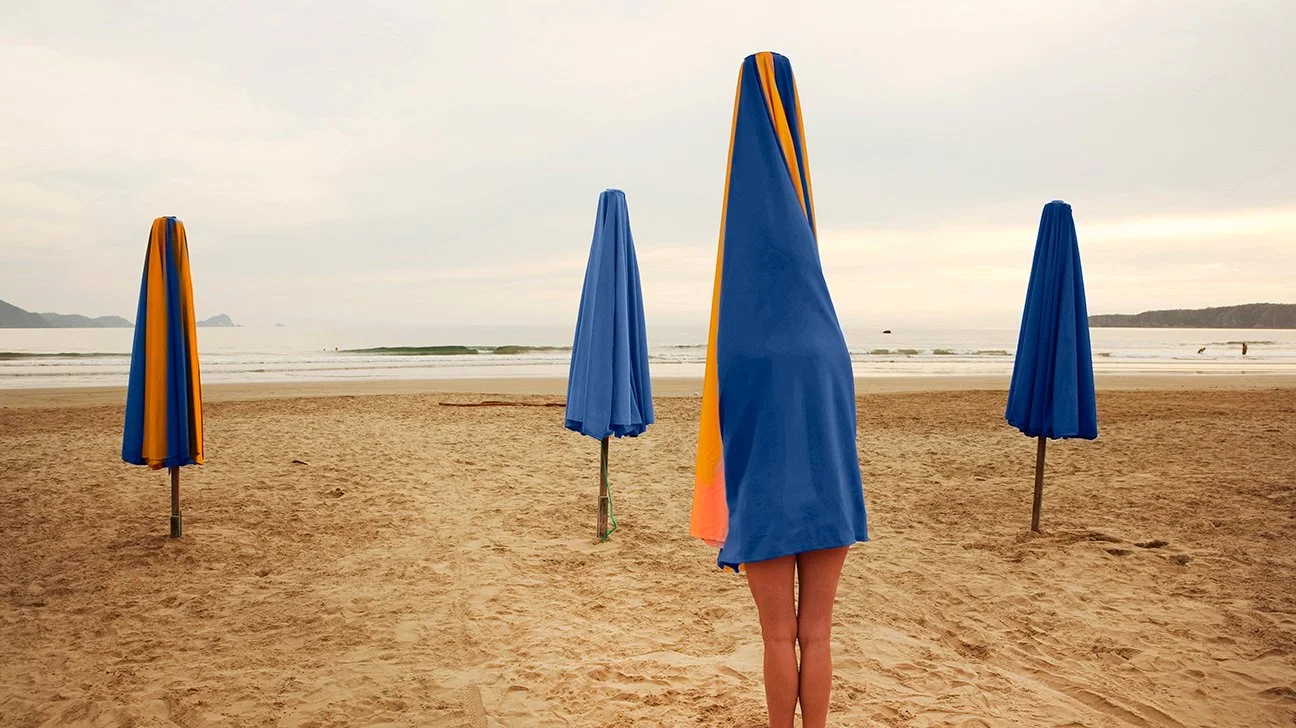 person-hiding-underneath-beach-umbrella-sand-ocean-1296x728-header.jpg