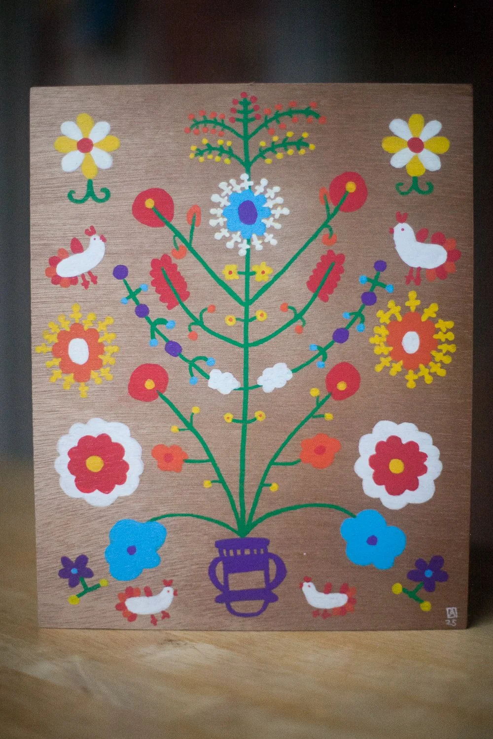 a wooden board with a brightly coloured drawing of flowers and chickens