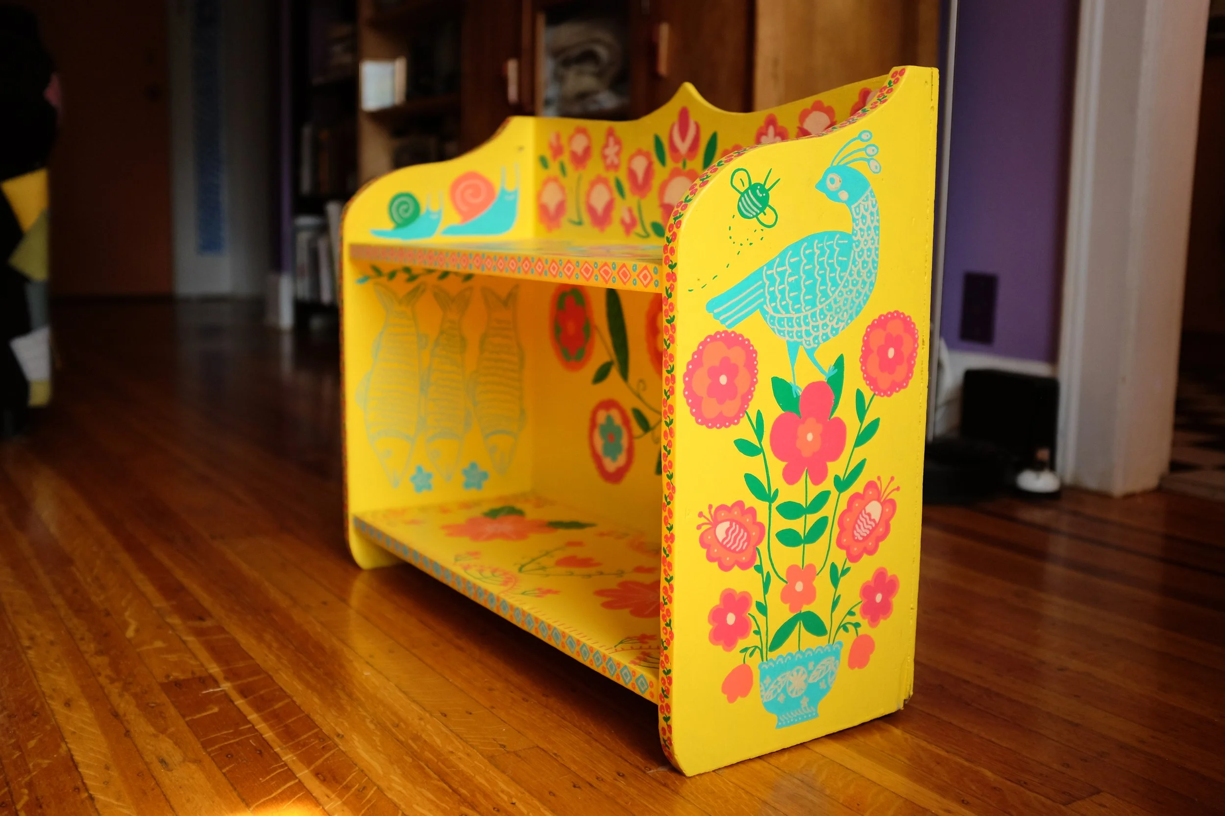 a yellow shelf with designs of birds and flowers