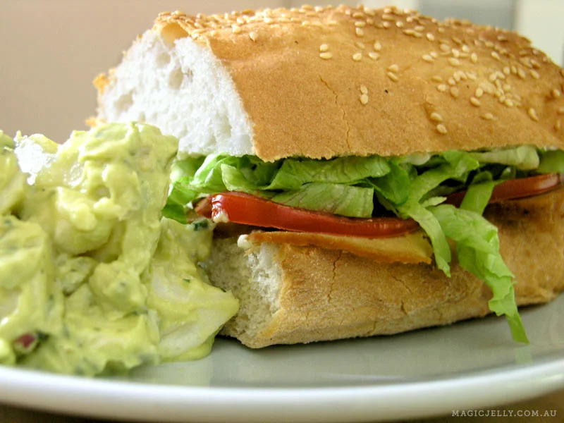 Homemade smokey seitan and salad on a crusty roll with a side of avocado potato salad.