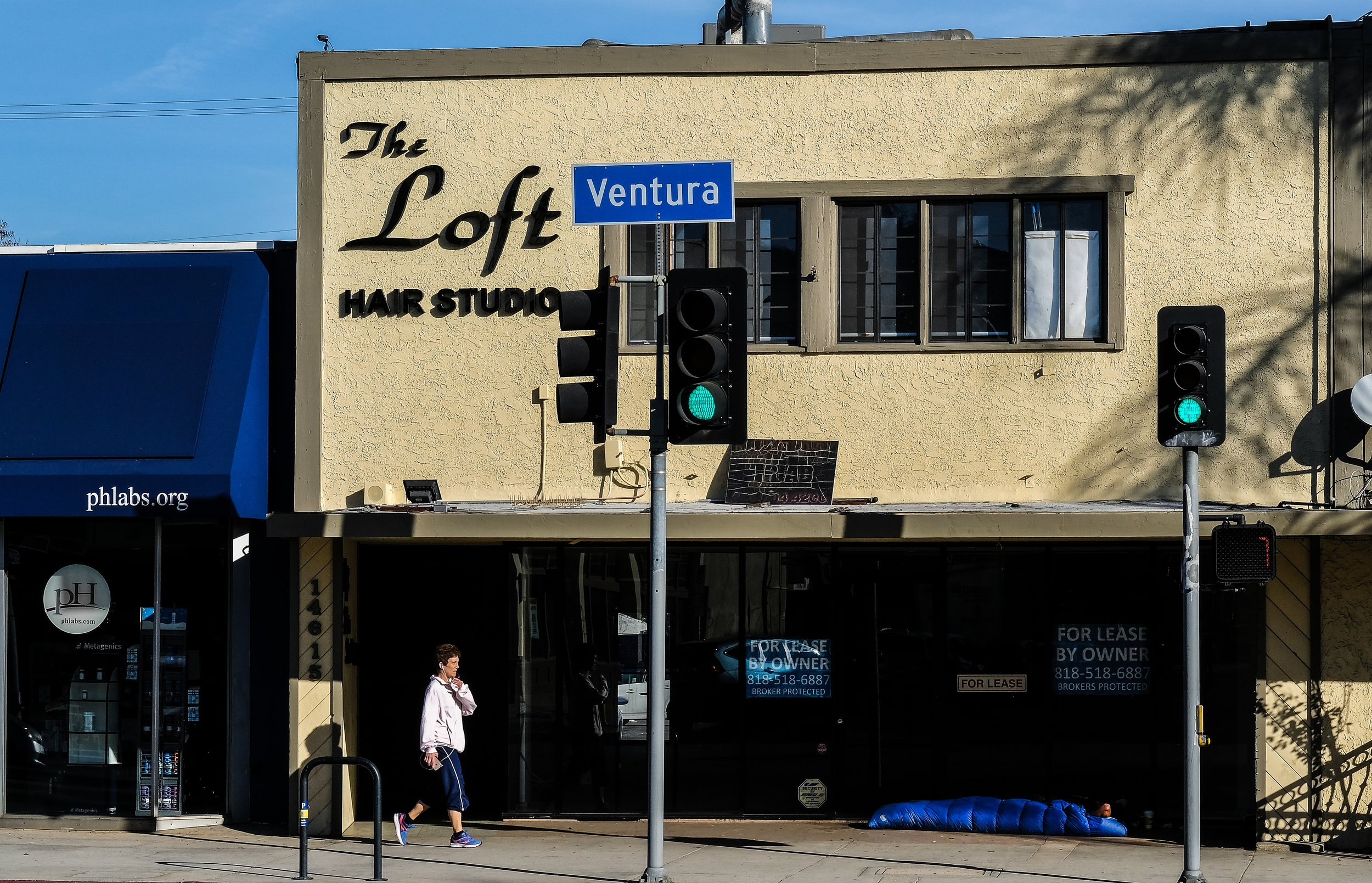  A woman walking along Ventura Blvd passes by Nic sleeping in front of an empty retail space in Sherman Oaks, CA. 