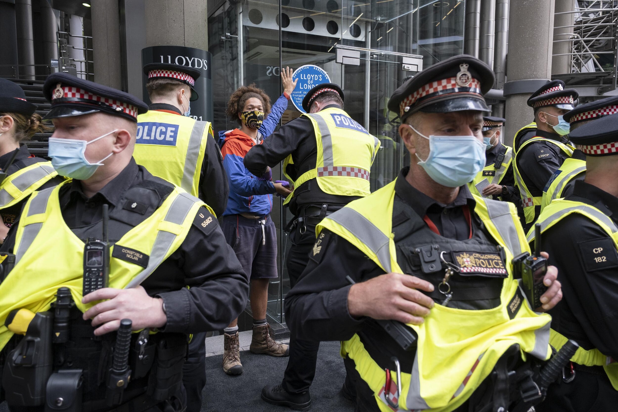  Police talk to a young man who has glued his hand on a blue plaque which talks of links to slavery and fossil fuel projects pasted up outside the Lloyd's of London during the Walk of Shame disruptive march through the City of London. 