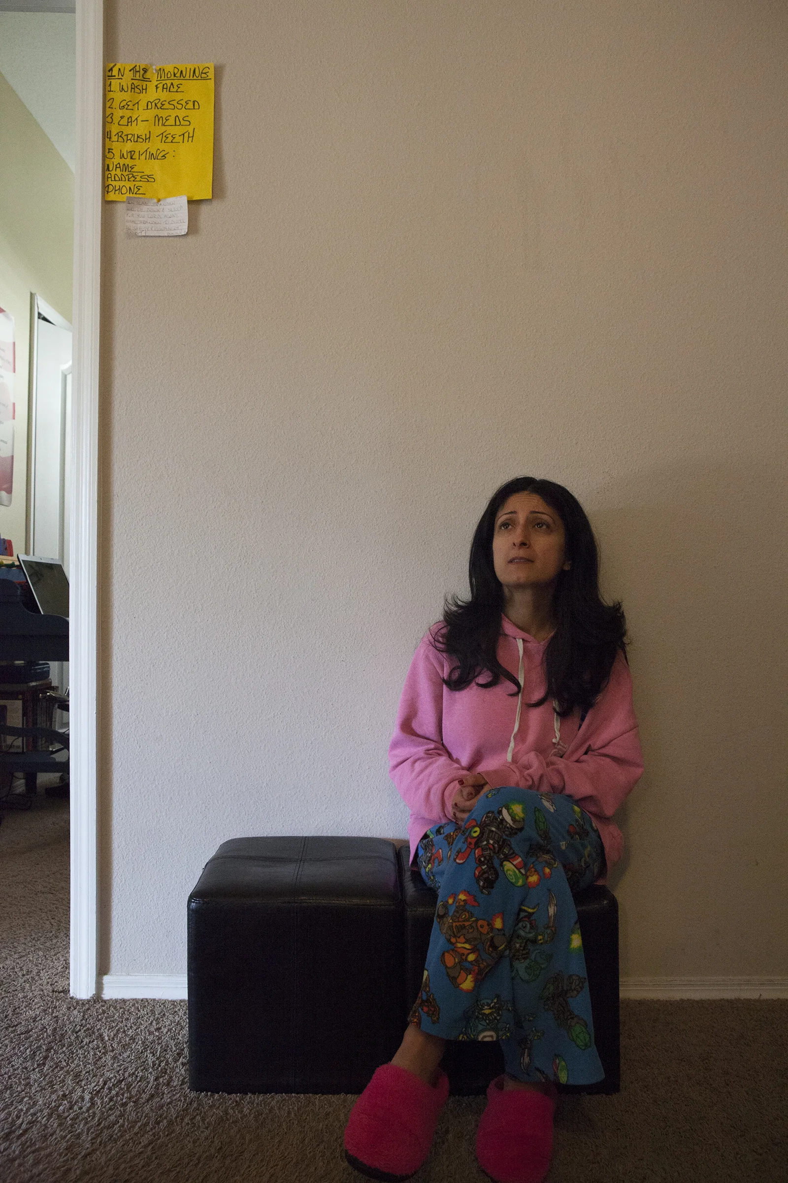 Renee in the early morning, sitting outside of Branden's room. Above Renee on the yellow sheet of paper, is a list of things for Branden to remember to do in the morning; wash his face, get dressed, take his meds, brush his teeth, and to write his name, address, and phone number. Tampa, FL.