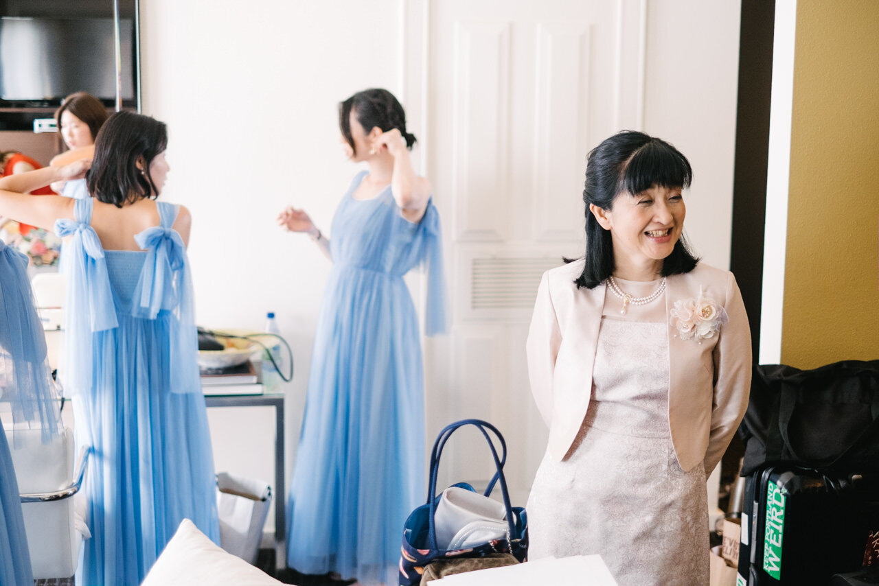  Mother of bride smiling while bridesmaids get ready in blue dresses 