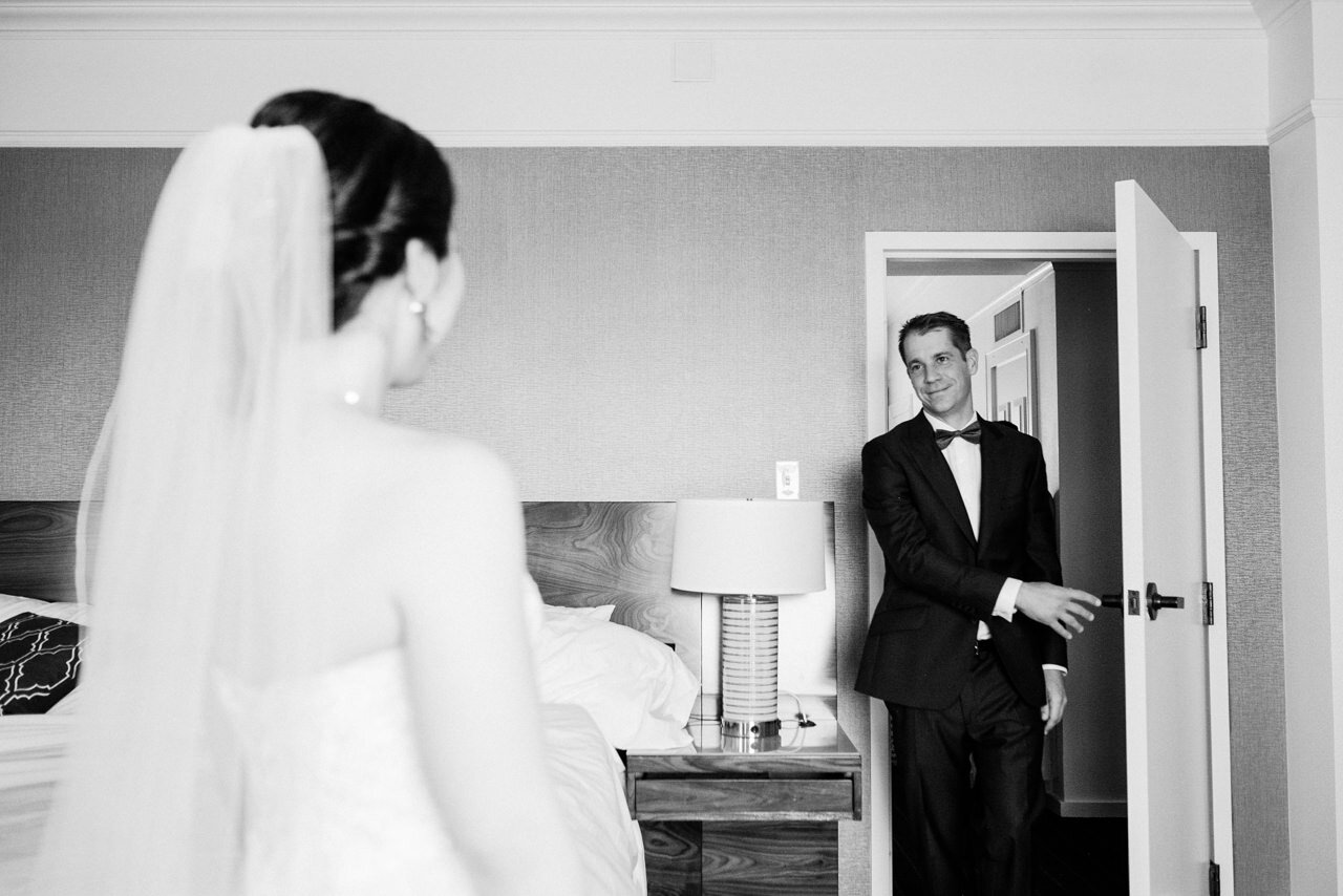  Groom walks in hotel room door seeing bride in wedding dress 