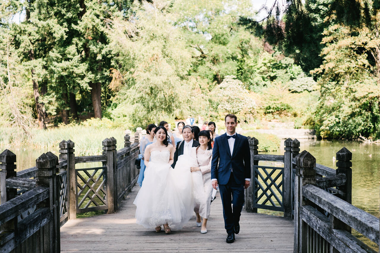  Bride, groom and wedding party cross bridge towards wedding ceremony at crystal springs rhododendron garden 