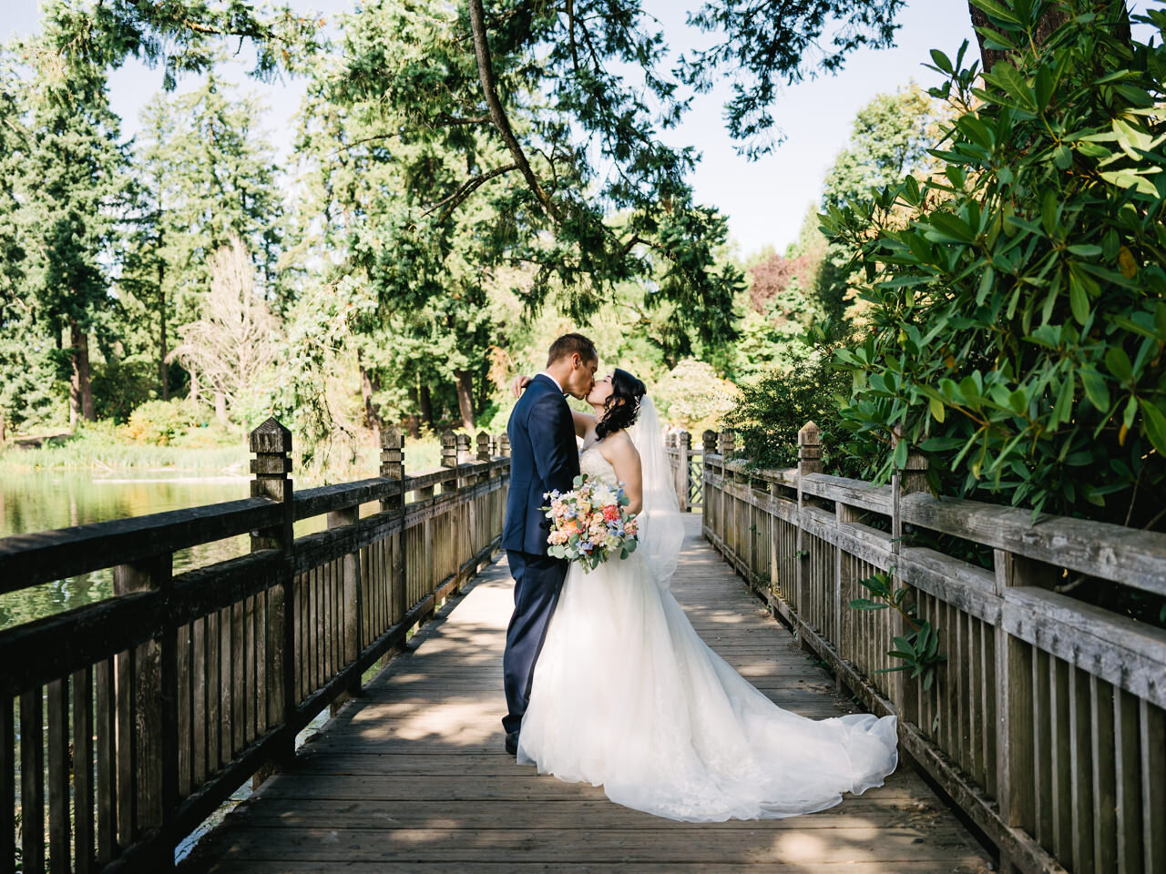  Bride and groom kiss on wooden walkway under large tree branches at crystal springs rhododendron garden 