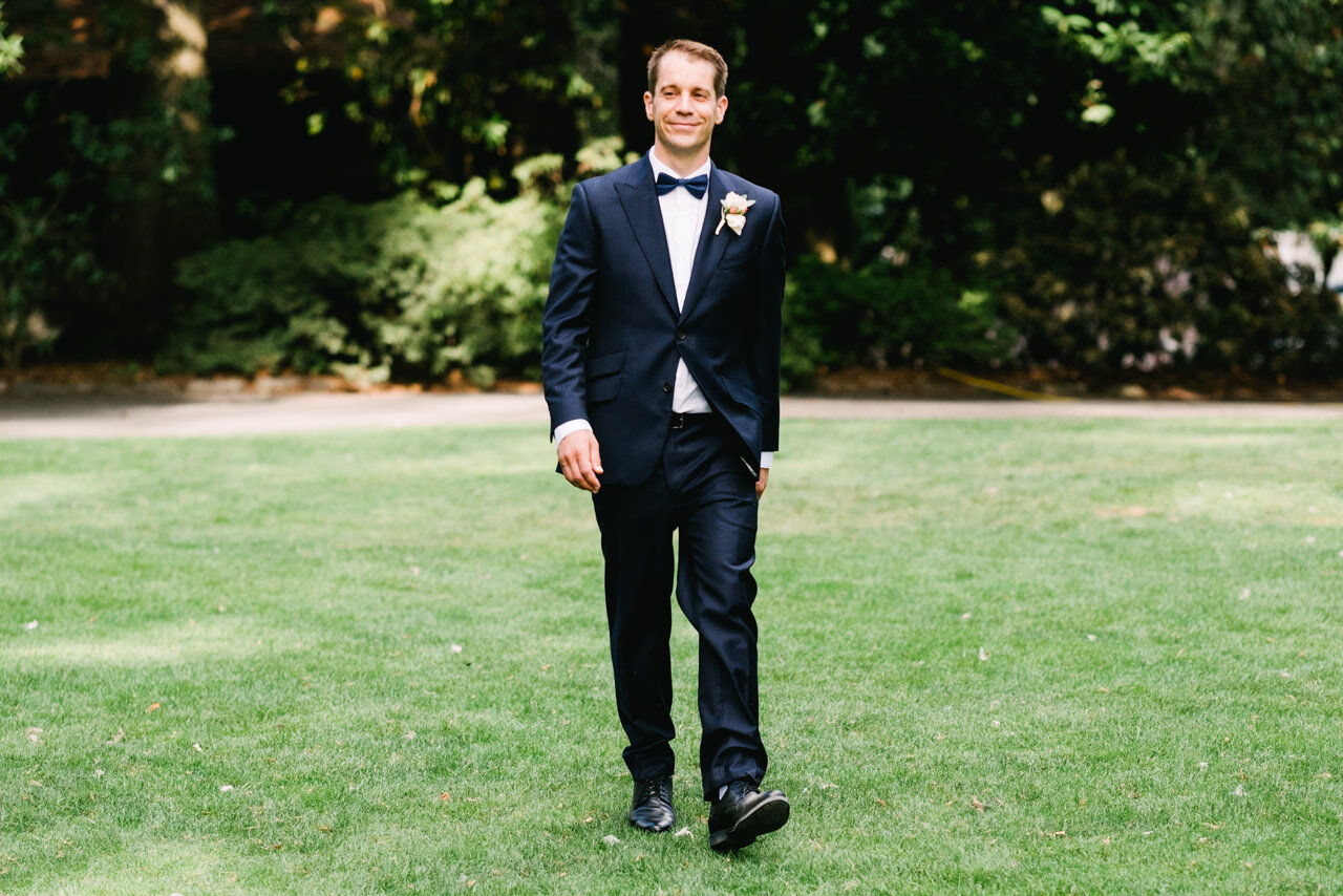  Groom with blue bow tie smiles while walking towards ceremony 