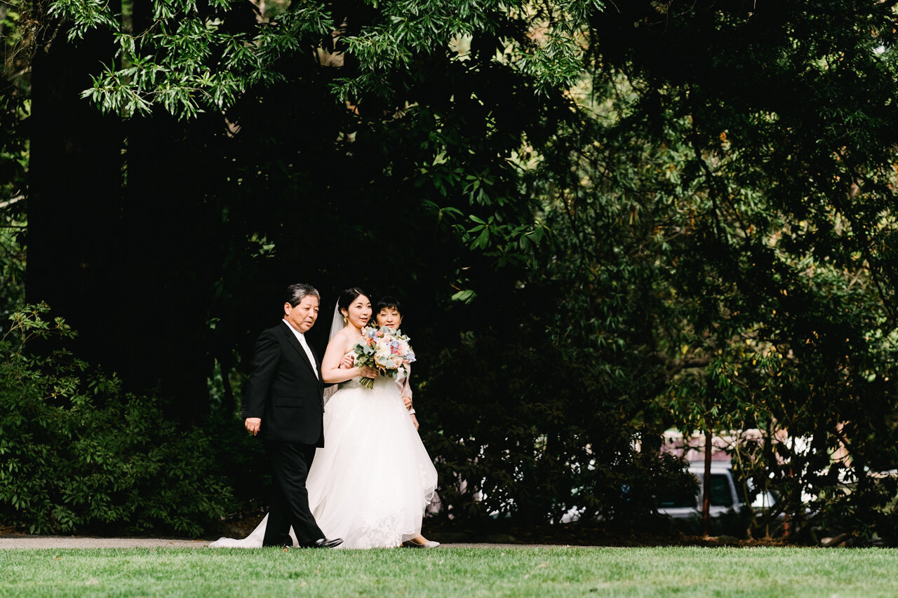  Bride walks together with mother and father approaching the lawn at crystal springs garden 