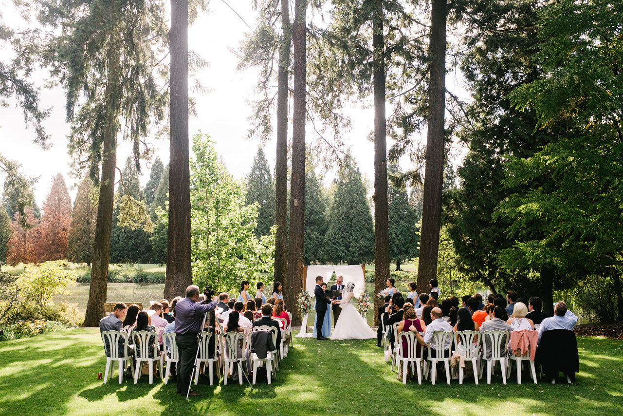  Wedding ceremony at crystal springs rhododendron garden on lawn in front of tall fir trees and pond 
